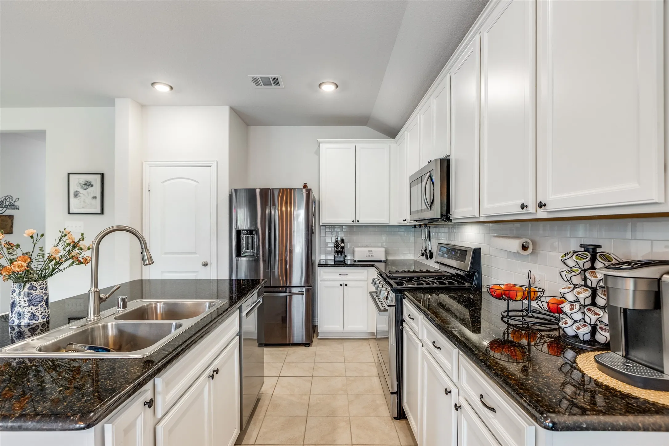 Kitchen featuring stainless steel appliances, backsplash, light tile patterned flooring, white cabinetry, and dark stone countertops