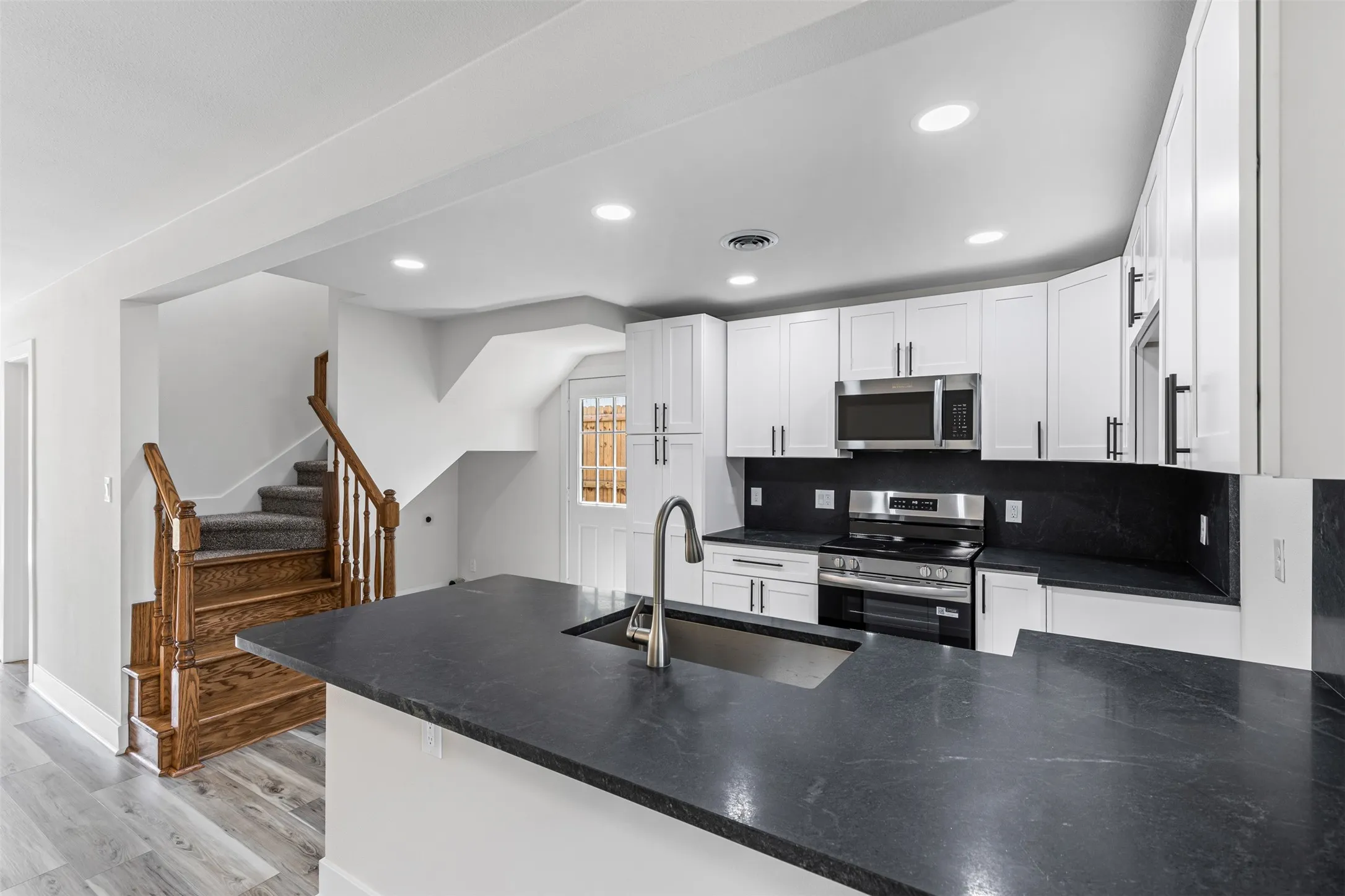 Kitchen with appliances with stainless steel finishes, light wood-type flooring, white cabinets, recessed lighting, and dark stone counters