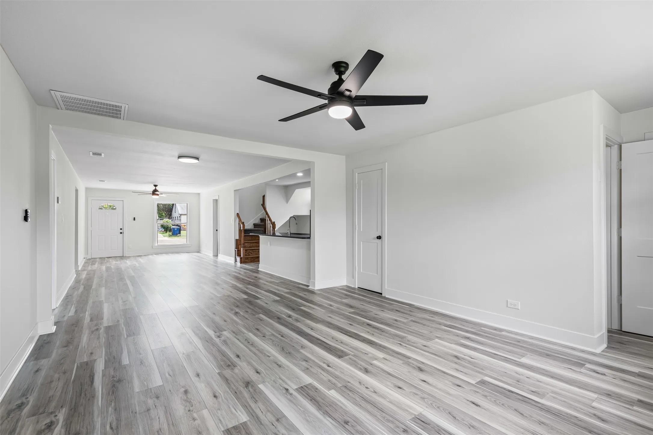 Unfurnished living room with ceiling fan, light wood-style floors, and stairs