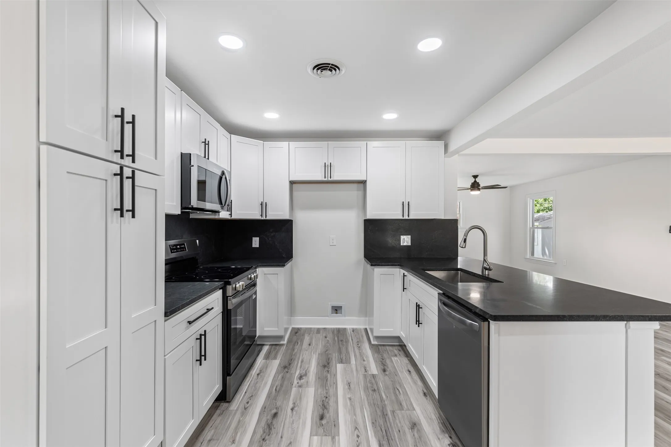 Kitchen with stainless steel appliances, ceiling fan, white cabinetry, light wood-style floors, and recessed lighting