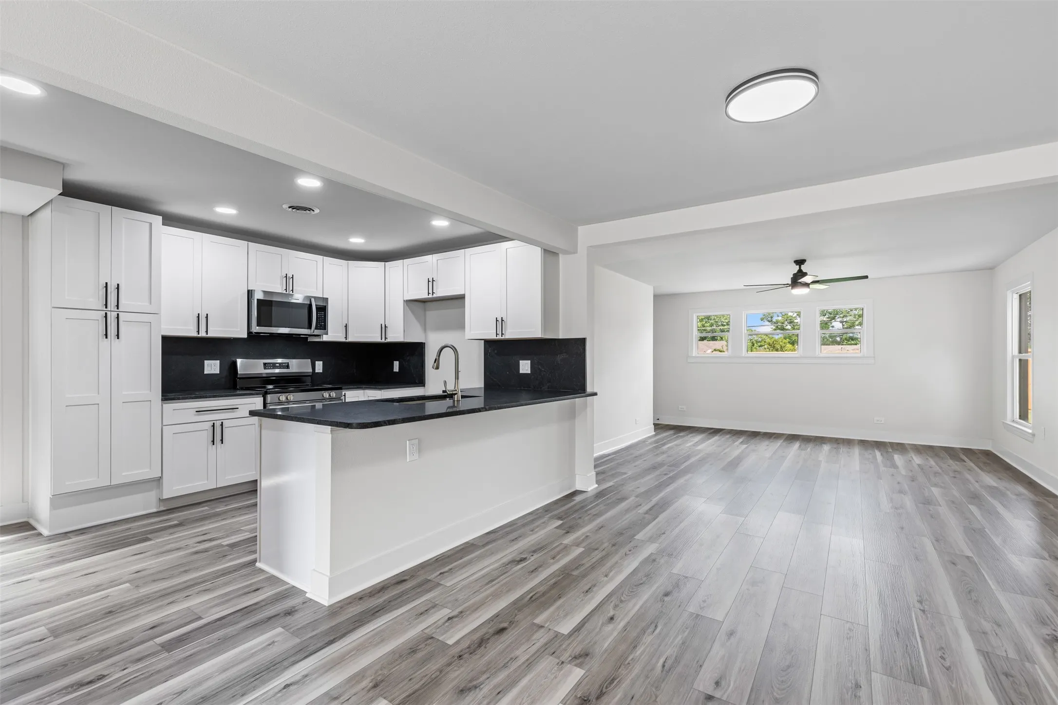 Kitchen with open floor plan, white cabinets, appliances with stainless steel finishes, backsplash, and a peninsula