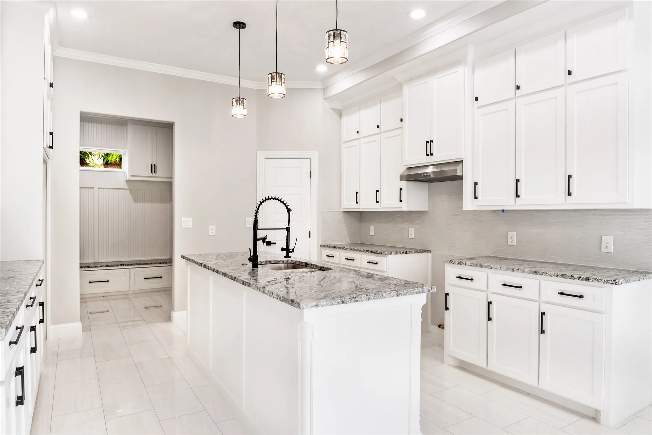 Kitchen with decorative backsplash, tons of custom solid wood cabinets with custom hardware and fixtures, crown and ornamental molding, light flooring, custom granite stone countertops, and extractor fan