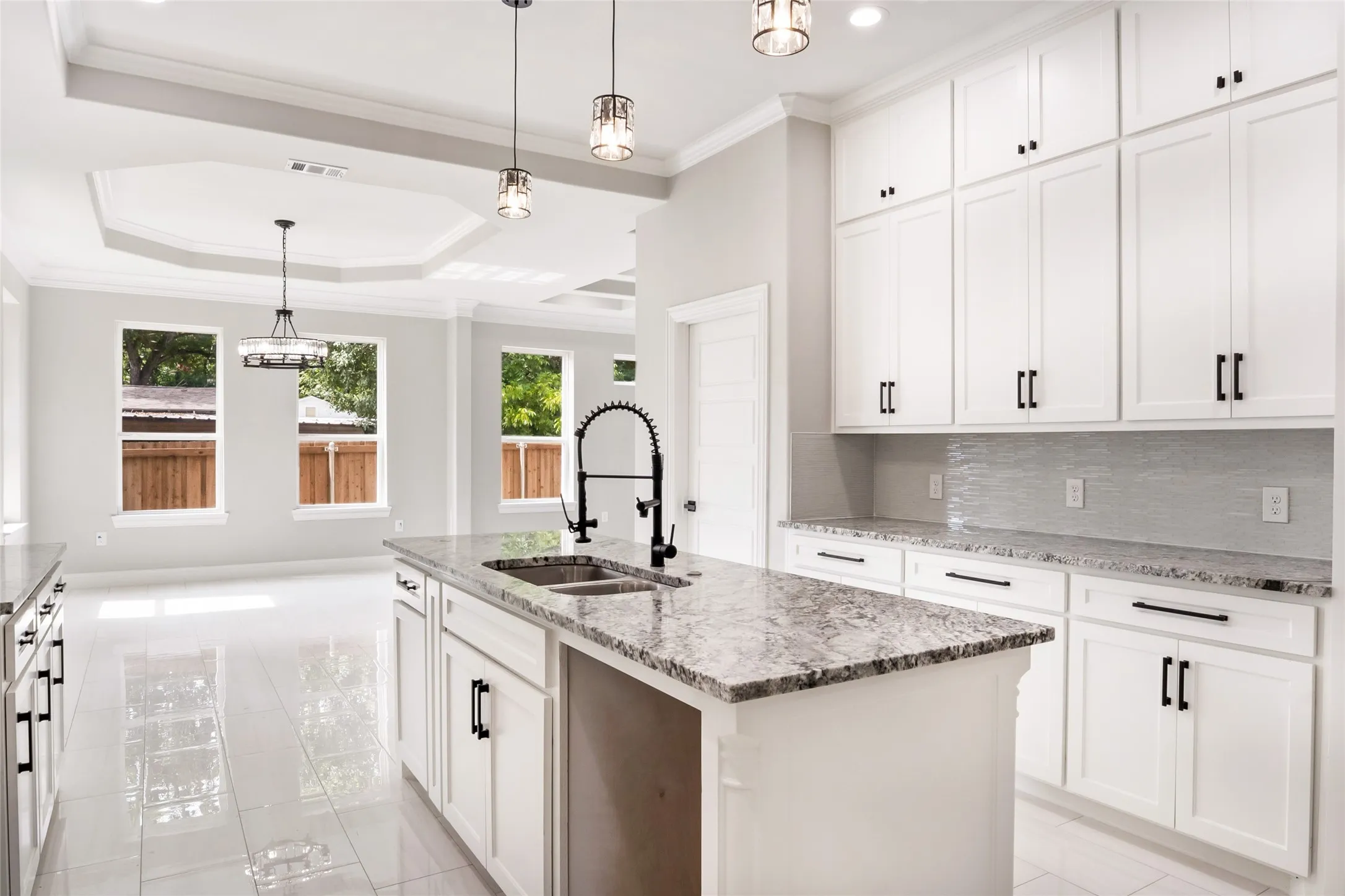Kitchen featuring backsplash, a tray ceiling, crown molding, light tile patterned floors, and light stone counters