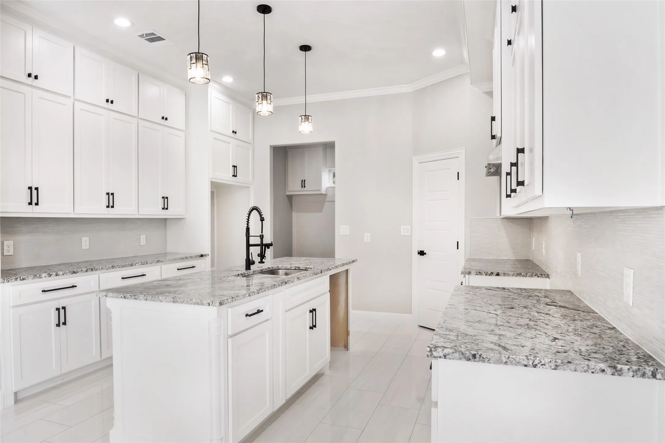 Kitchen with  backsplash, custom granite countertops, crown molding, a center island with custom fixtures, hardware and sink, and custom solid wood white cabinets
