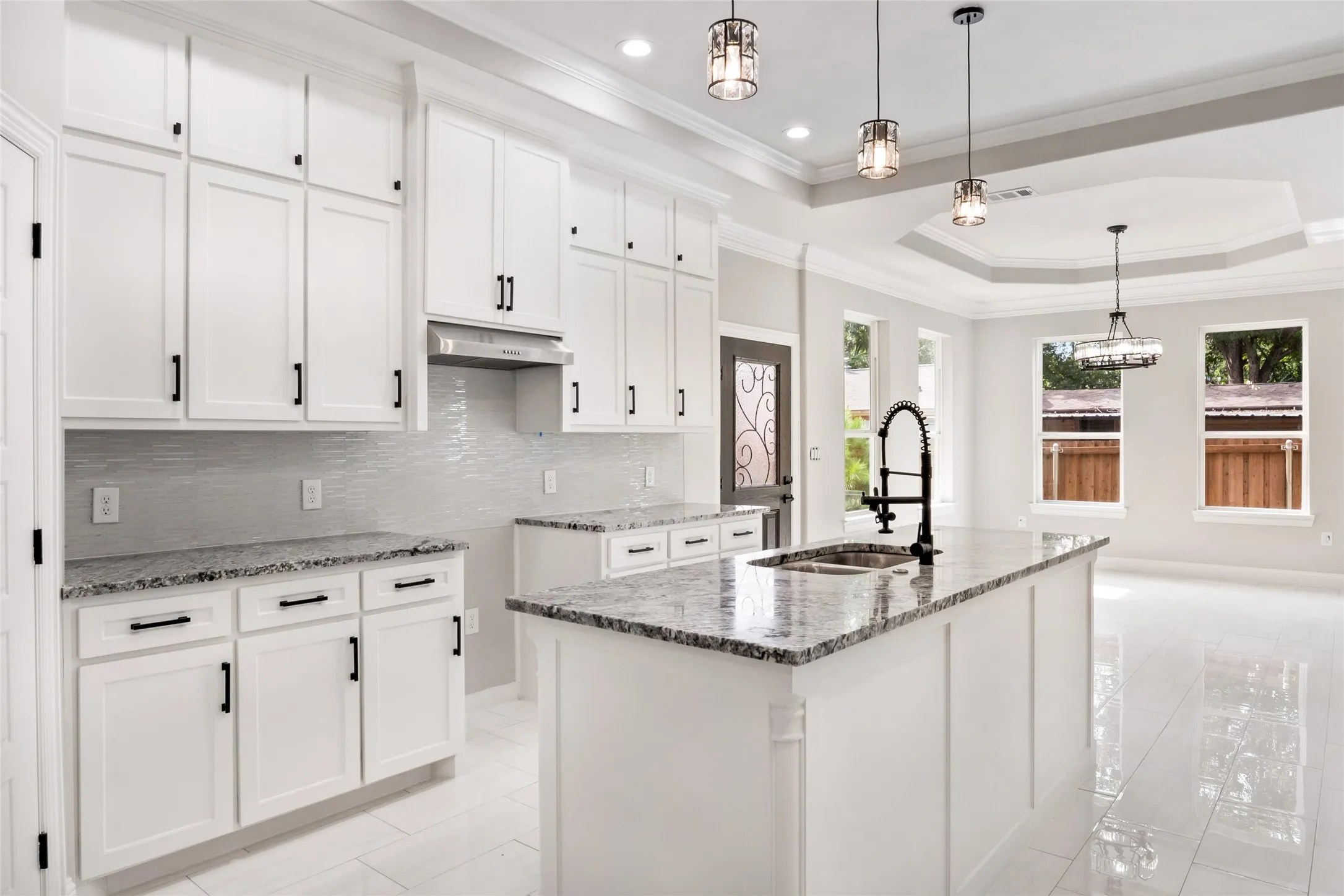 Kitchen with a tray ceiling, tasteful backsplash, custom solid wood cabinets, custom granite stone counters, crown molding, and custom solid wood white cabinetry