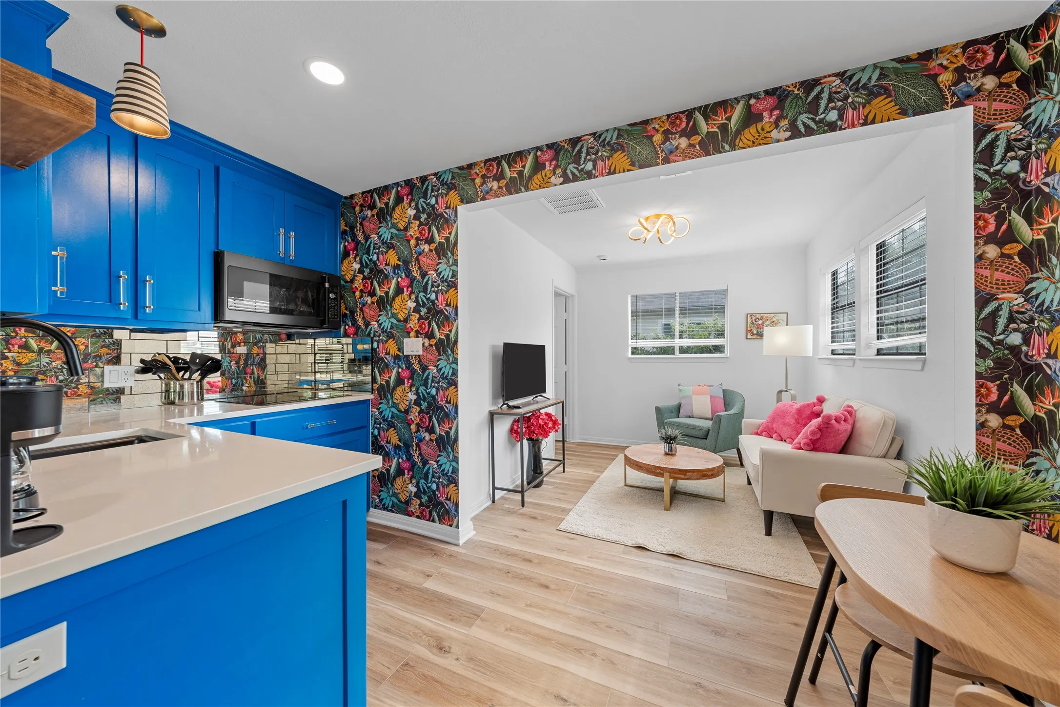 Kitchen featuring wallpapered walls, blue cabinetry, light wood finished floors, tasteful backsplash, and decorative light fixtures