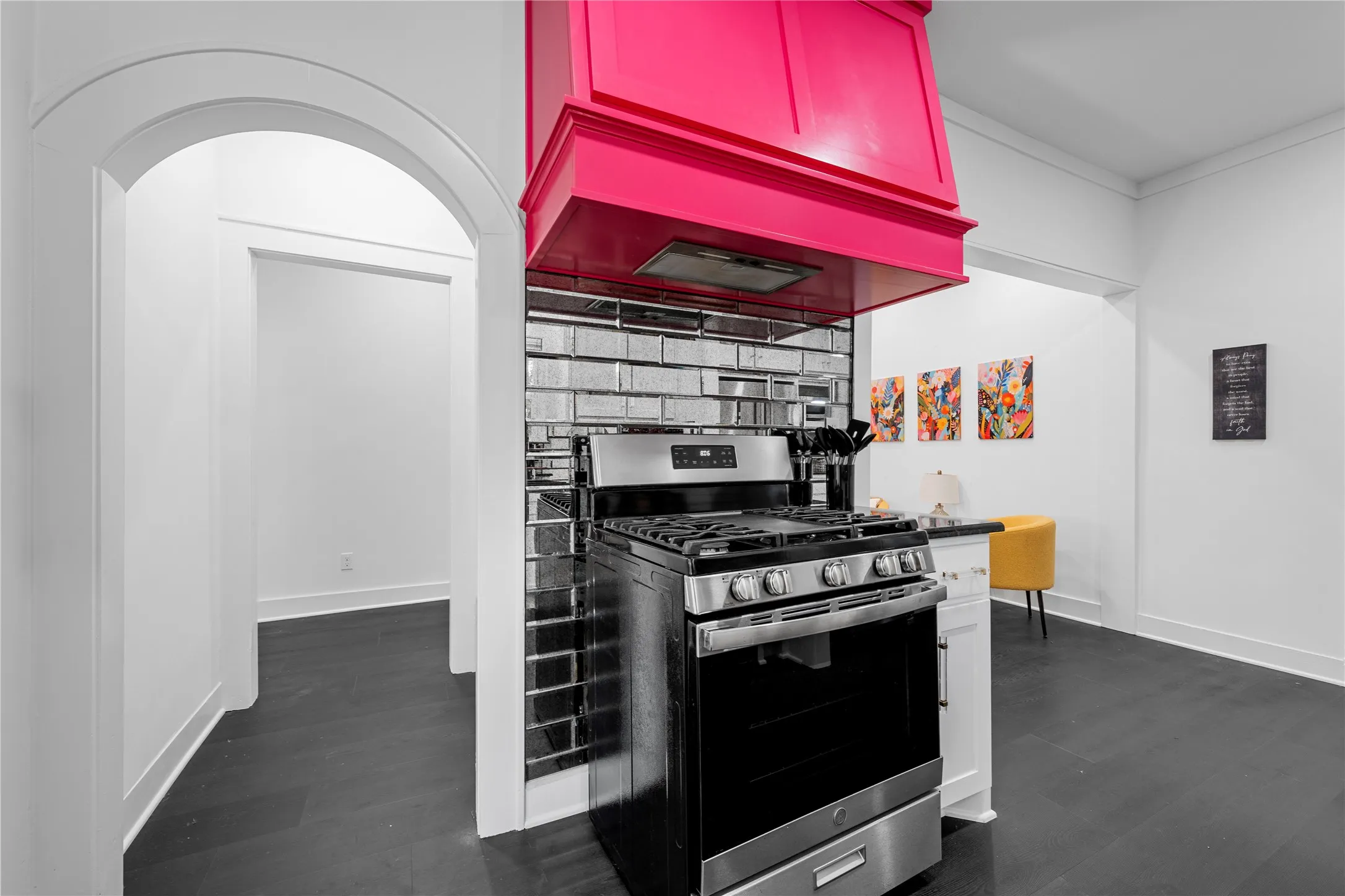 Kitchen with stainless steel range with gas stovetop, custom exhaust hood, dark wood-type flooring, tasteful backsplash, and arched walkways