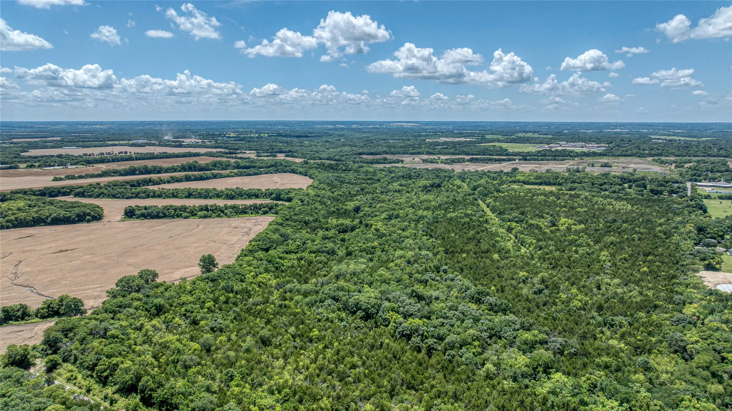 Aerial view of sparsely populated area featuring a heavily wooded area and farmland