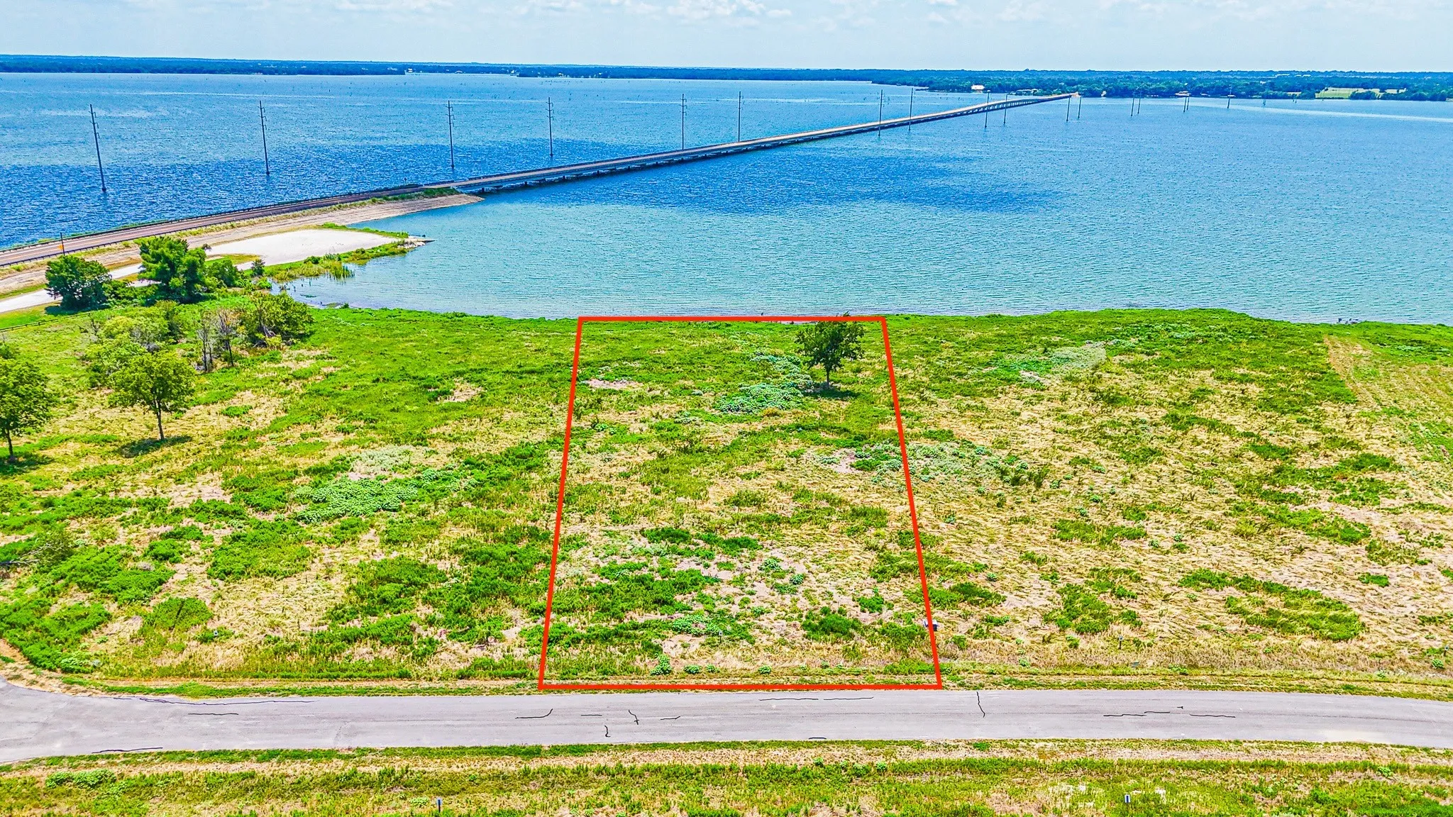 Aerial view of property and surrounding area with a nearby body of water, property parcel outlined, and a notable bridge
