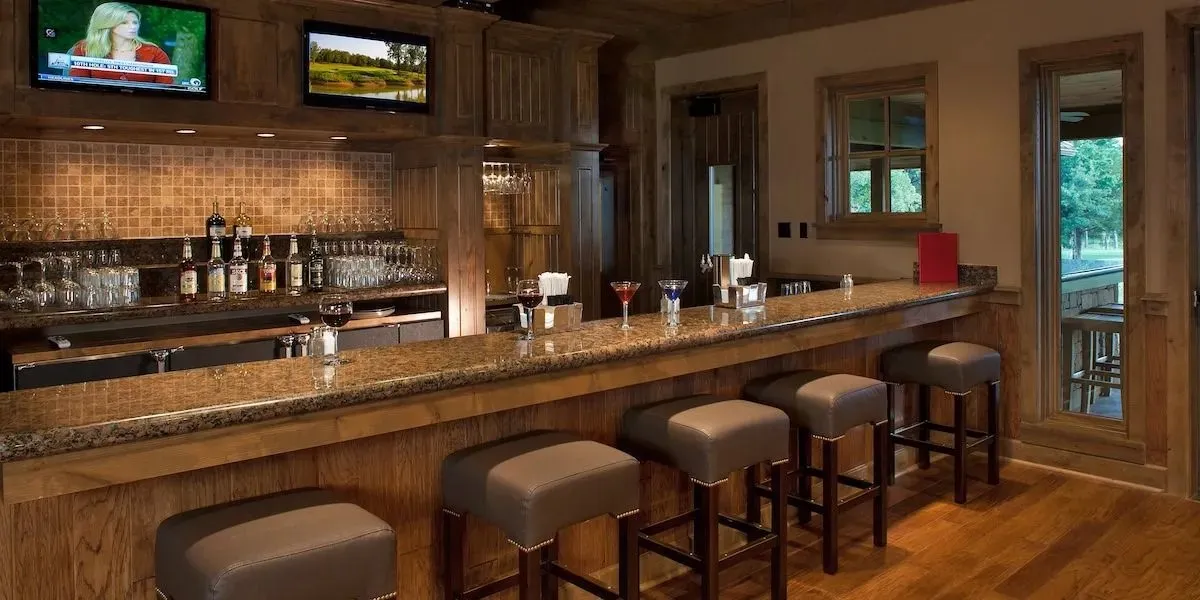 Indoor wet bar with wood finished floors, dark stone countertops, decorative backsplash, and brown cabinets