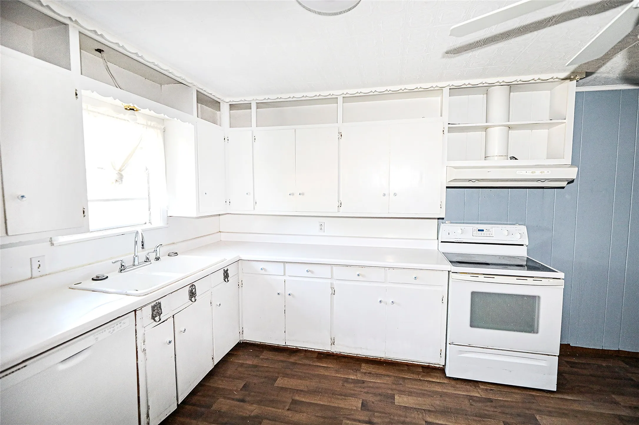Kitchen featuring white appliances, light countertops, white cabinetry, dark wood finished floors, and wood walls