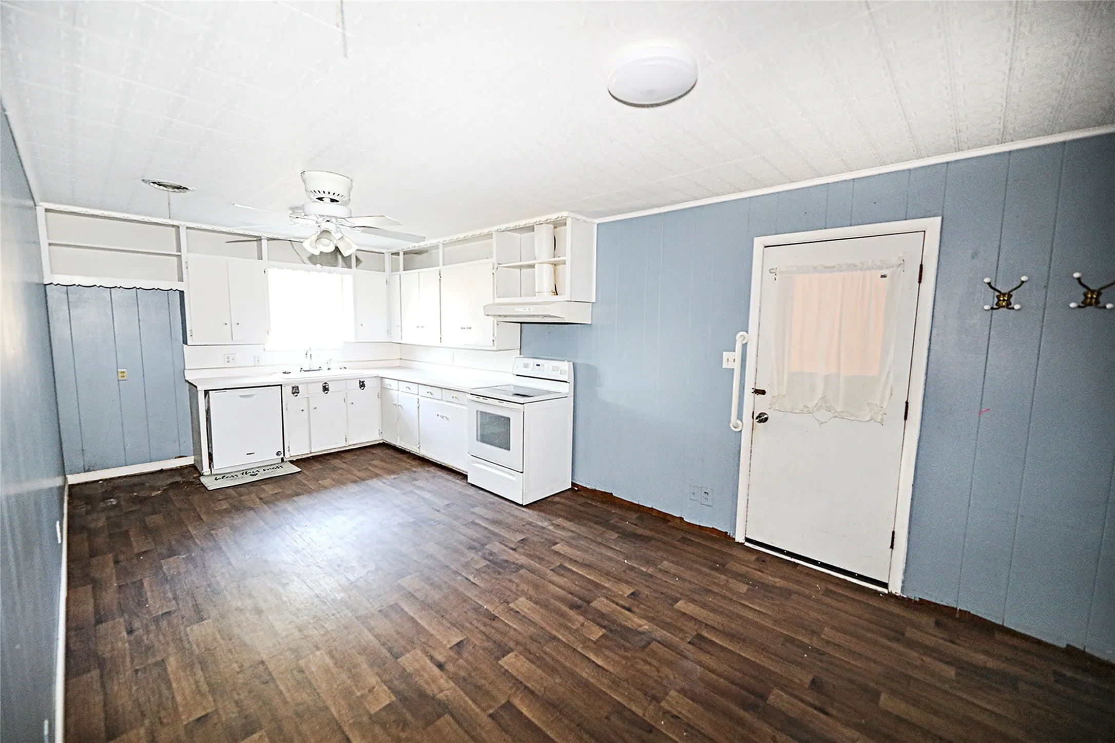 Kitchen with white cabinets, dark wood-style flooring, wooden walls, white appliances, and light countertops