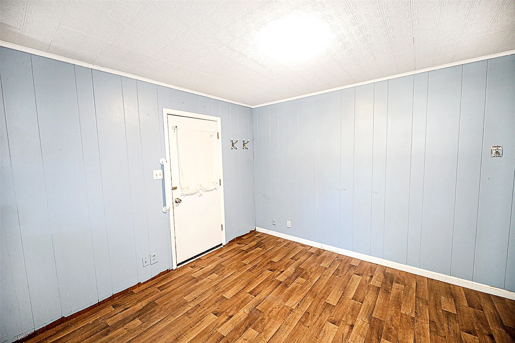 Unfurnished room with an ornate ceiling, wooden walls, wood finished floors, and ornamental molding