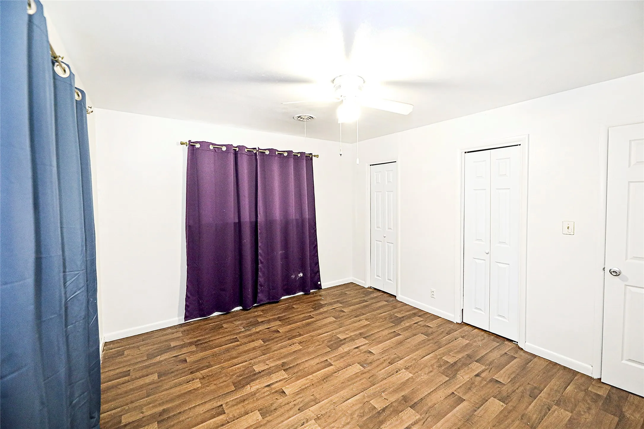 Unfurnished bedroom with multiple closets, wood finished floors, and ceiling fan