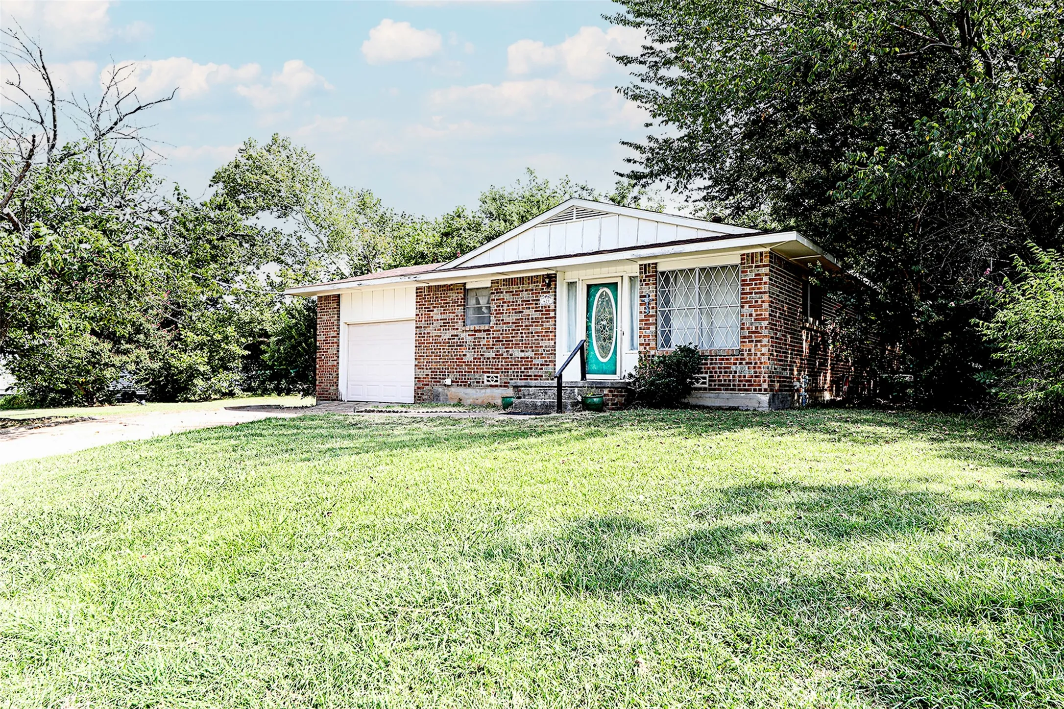 Ranch-style home with a front yard, a garage, concrete driveway, board and batten siding, and brick siding