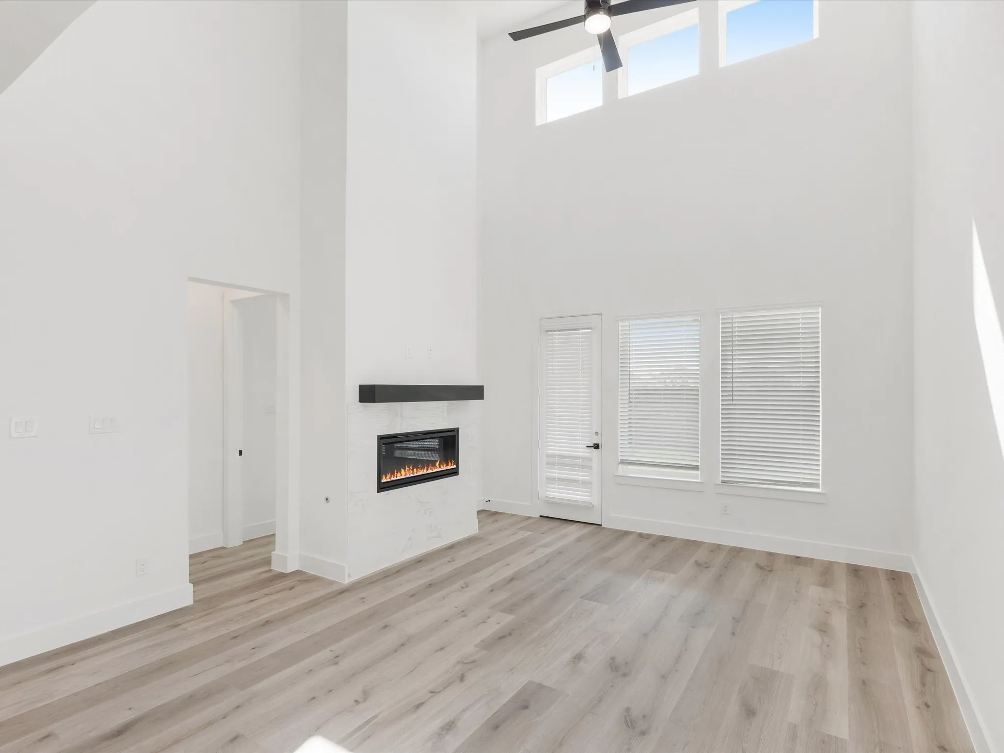 Unfurnished living room featuring a towering ceiling, light wood finished floors, a fireplace, and a ceiling fan