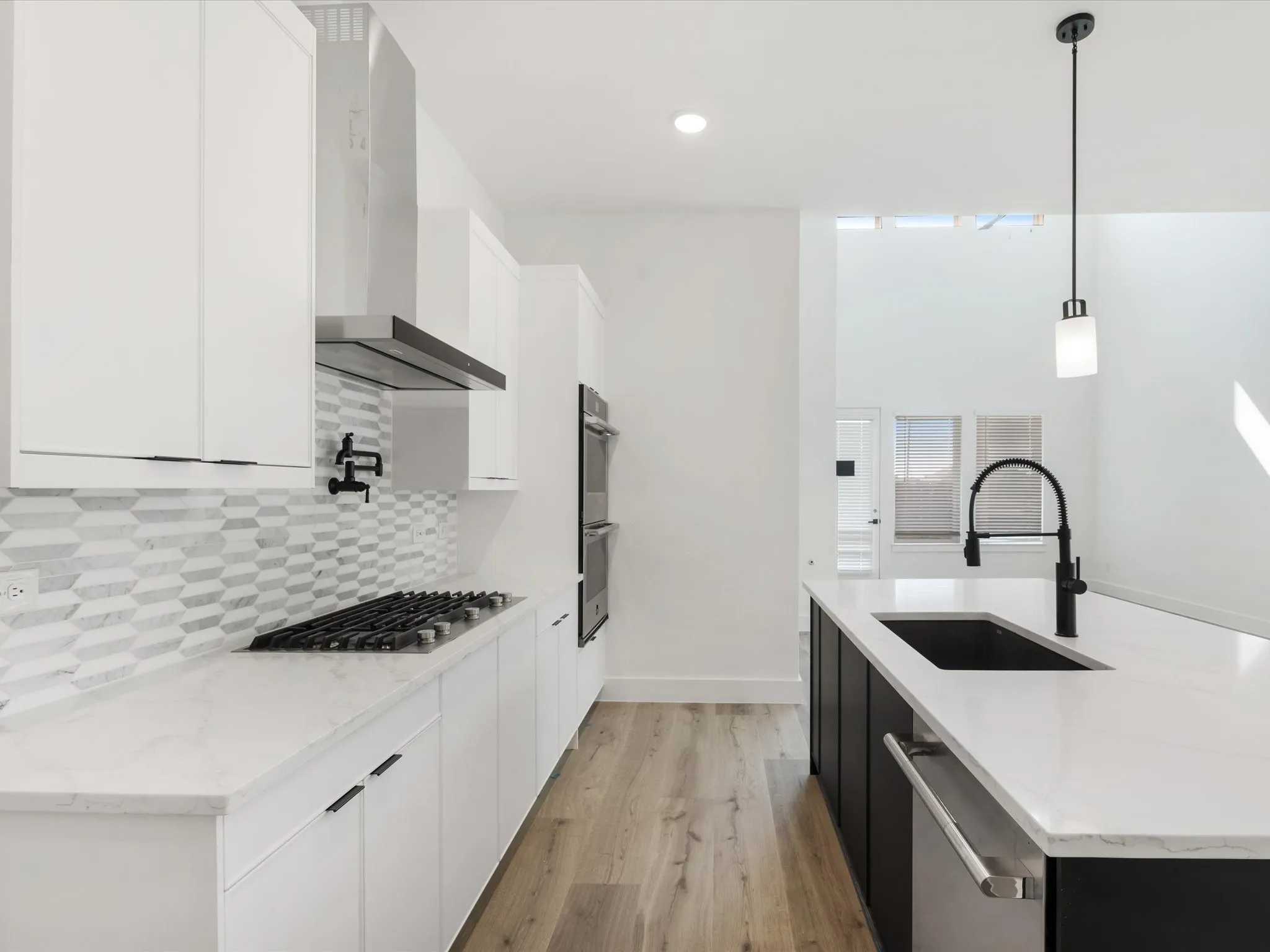 Kitchen featuring white cabinets, light stone counters, dark cabinetry, light wood finished floors, and wall chimney exhaust hood