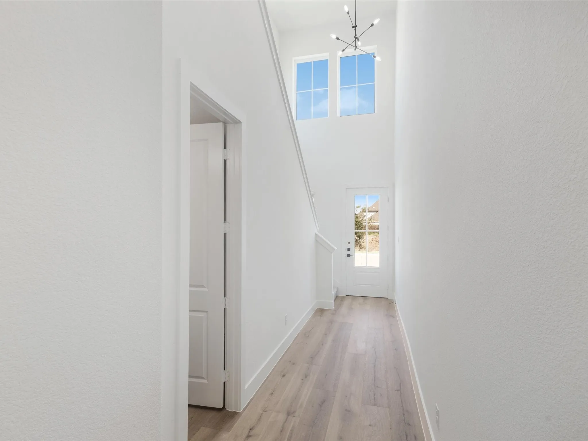 Hallway with light wood finished floors, a towering ceiling, and a chandelier