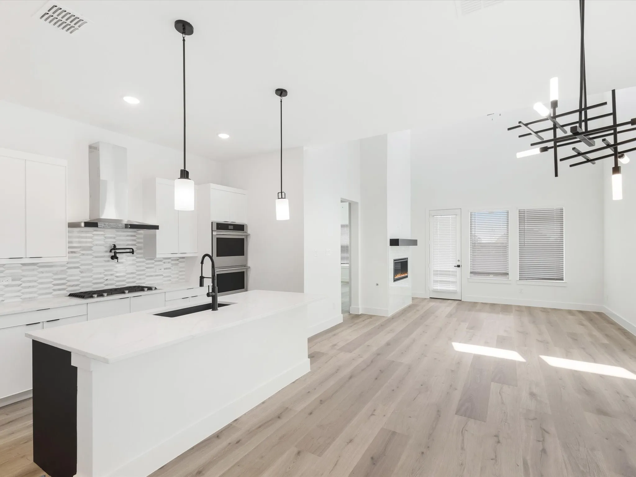 Kitchen featuring white cabinets, decorative light fixtures, a center island with sink, light wood-style flooring, and decorative backsplash