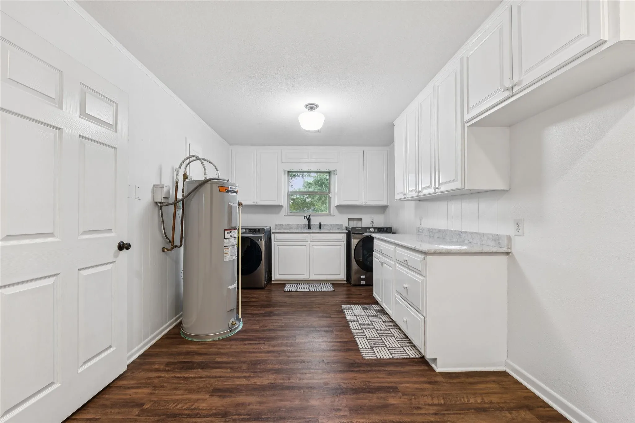Kitchen with white cabinets, light countertops, dark wood-style flooring, and electric water heater