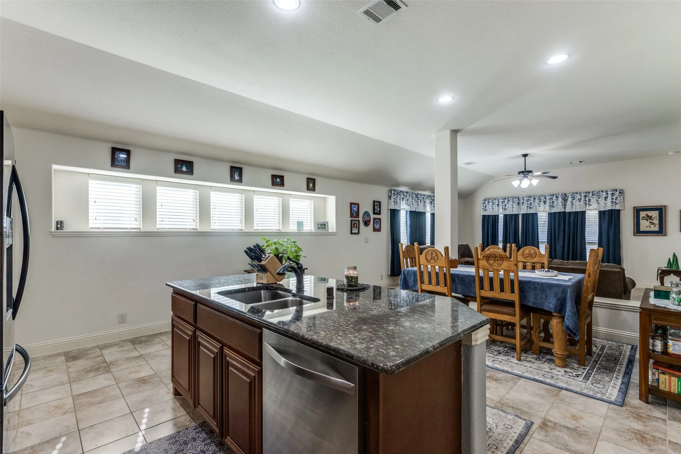 Kitchen featuring dark brown cabinets, dark stone countertops, stainless steel appliances, an island with sink, and ceiling fan