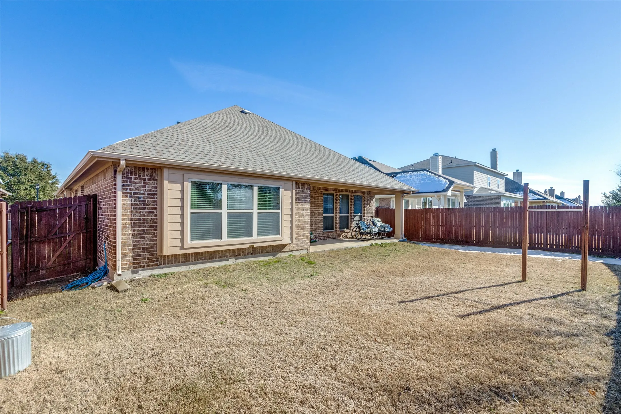 Rear view of house with brick siding, a fenced backyard, roof with a patio & entrance to jogging and bike trails.