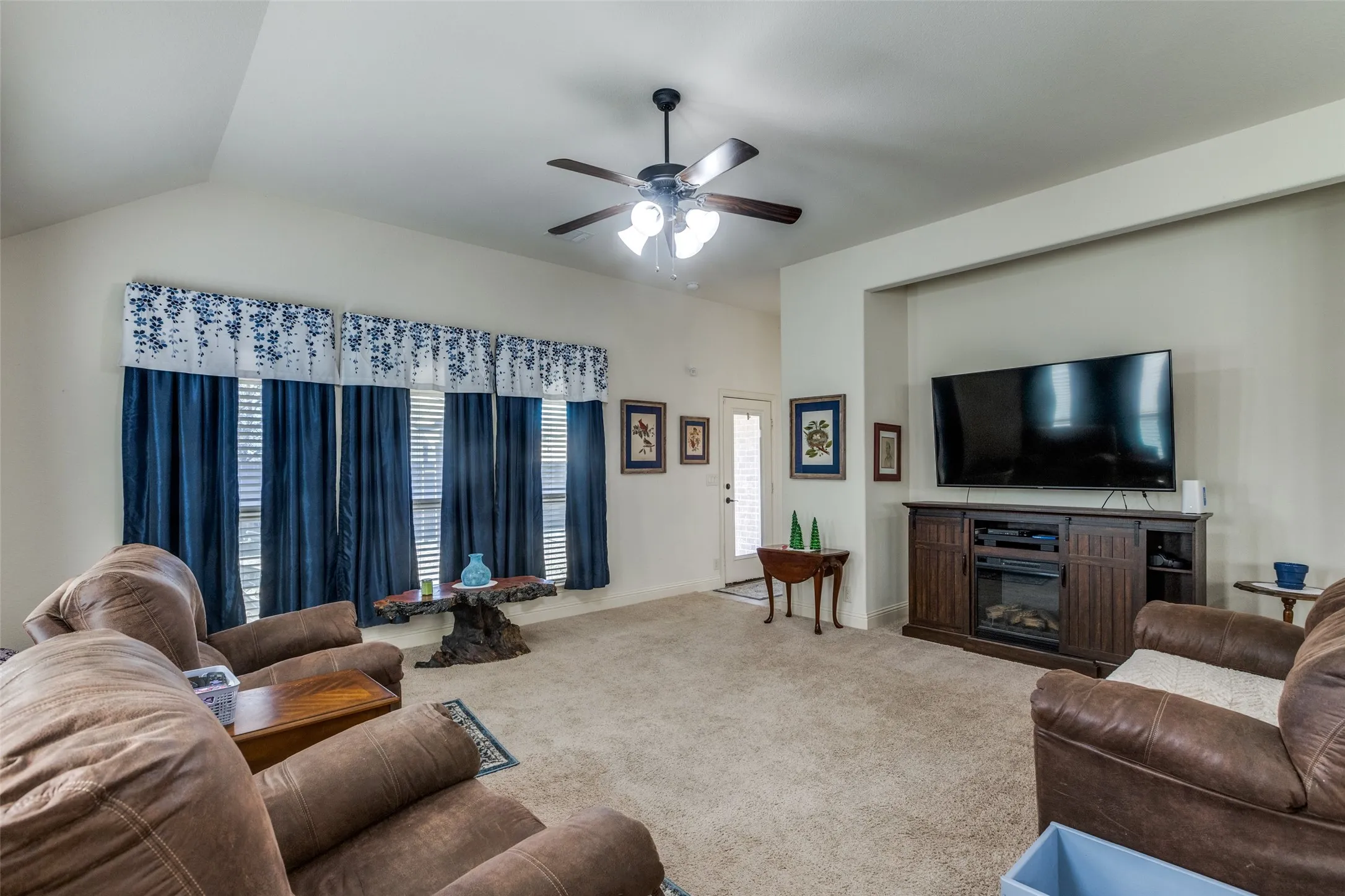Carpeted living area with a glass covered fireplace and ceiling fan