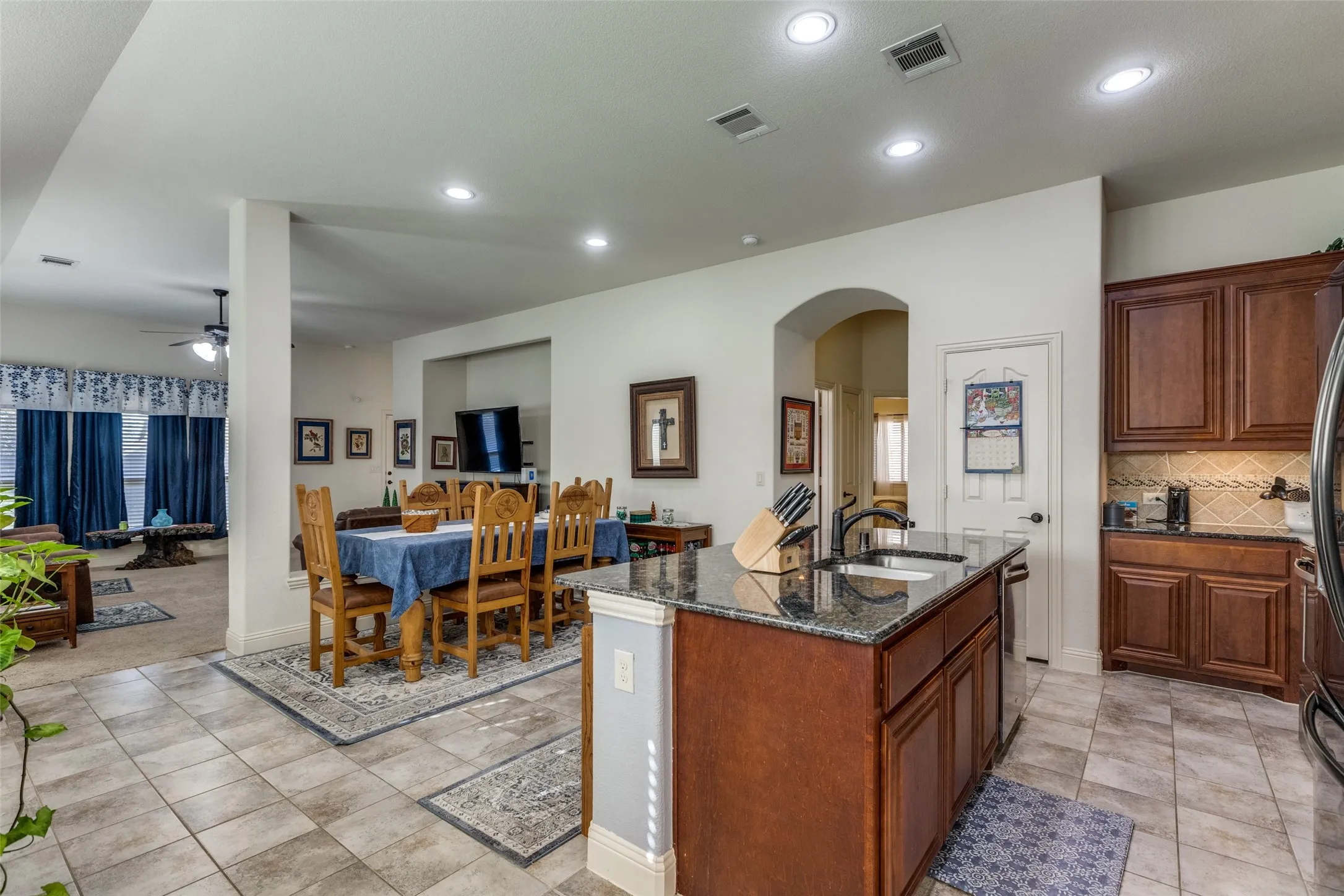 Kitchen featuring dark stone counters, recessed lighting, backsplash, ceiling fan, and an island with sink