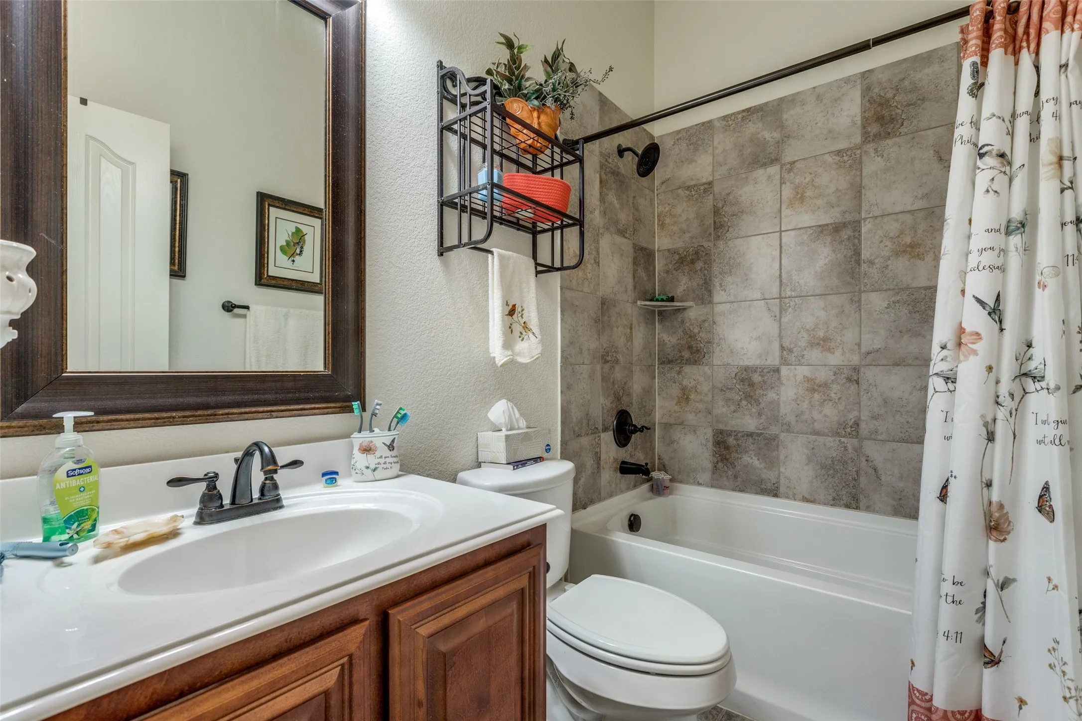 Full bathroom featuring shower / bath combo with shower curtain, a textured wall, and vanity