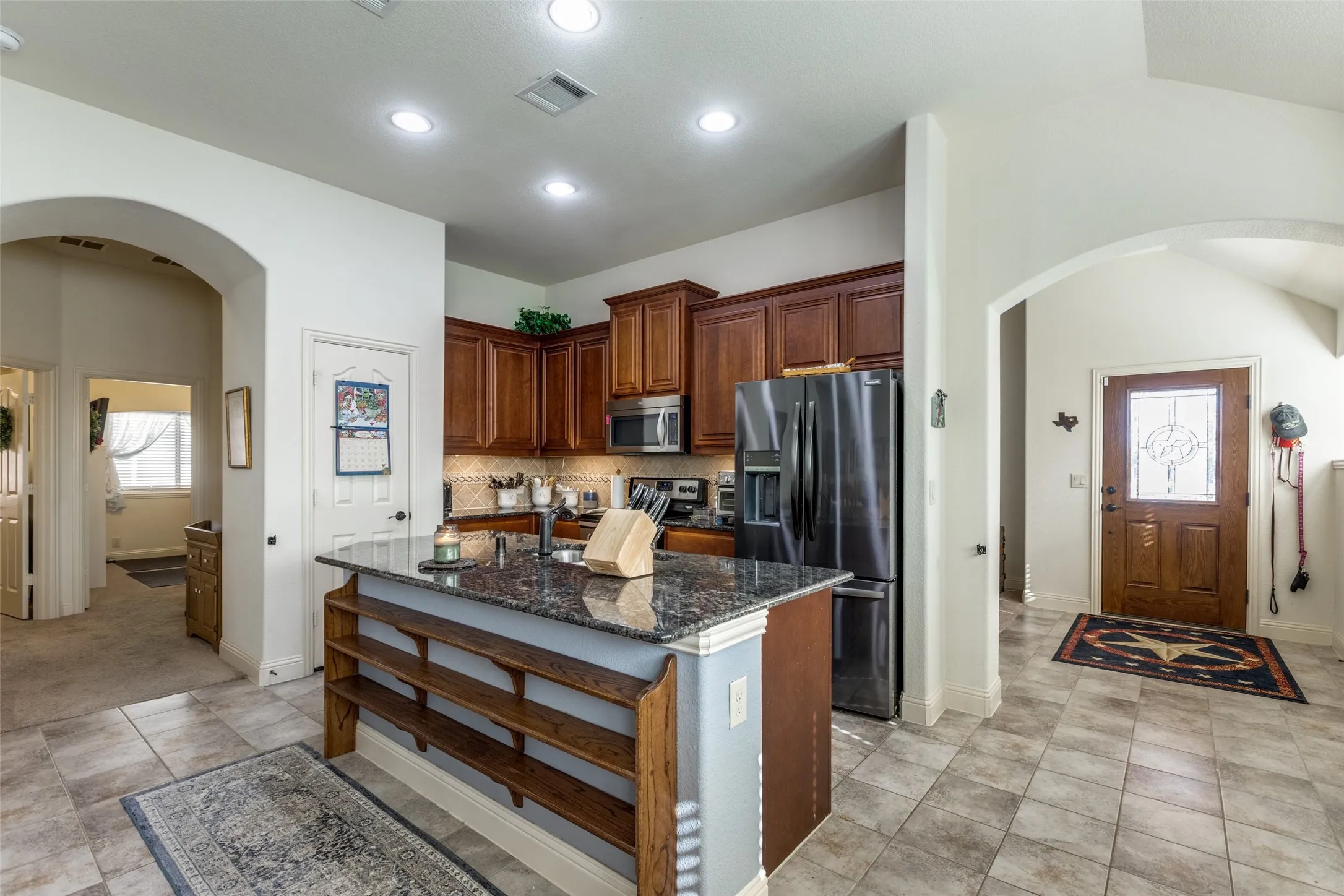 Kitchen featuring arched walkways, plenty of natural light, dark stone countertops, an island with sink, and recessed lighting