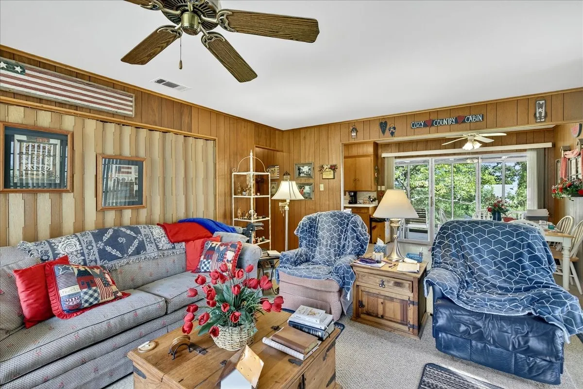 Carpeted living room featuring a ceiling fan and wooden walls
