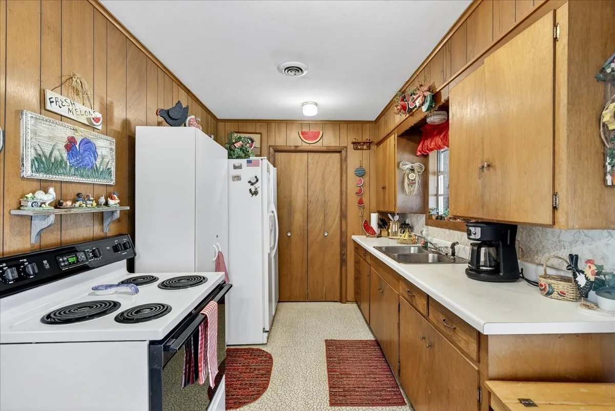 Kitchen featuring white appliances, light countertops, wooden walls, and brown cabinets