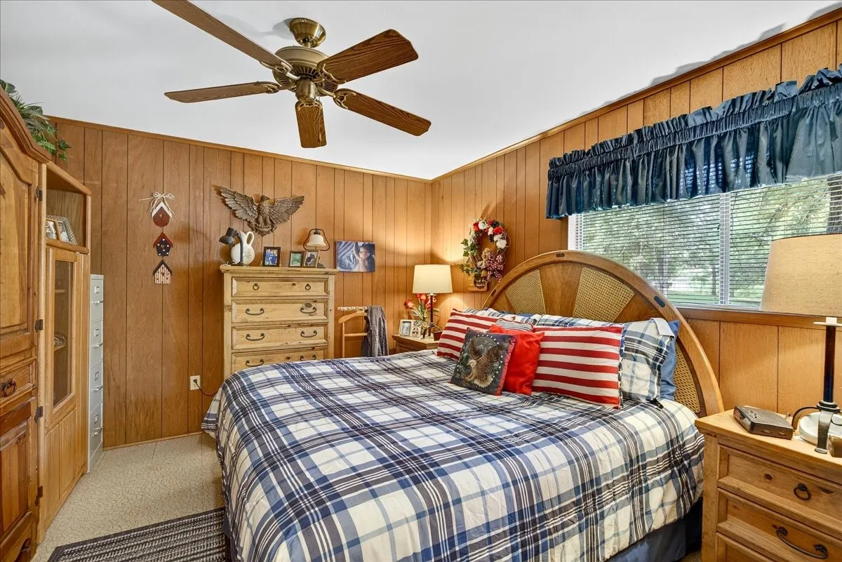 Bedroom with wood walls, light carpet, a ceiling fan, and crown molding