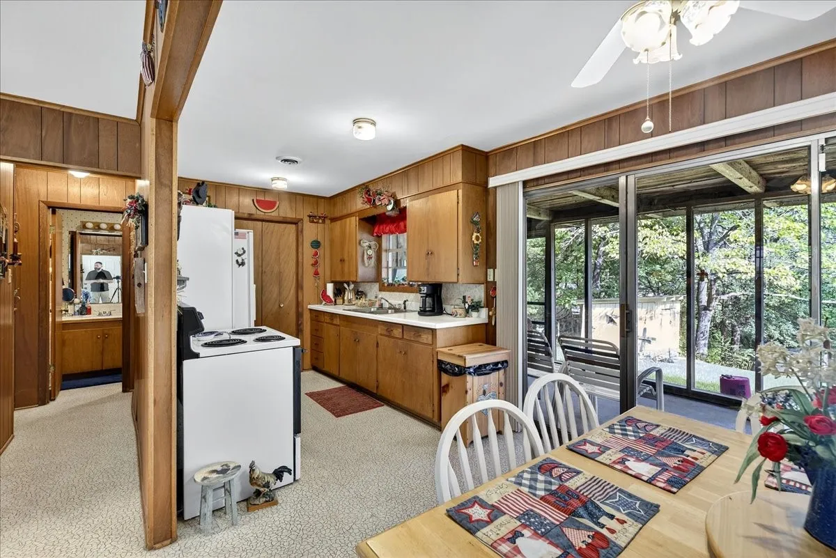 Kitchen with wooden walls, light countertops, white electric stove, brown cabinetry, and light colored carpet