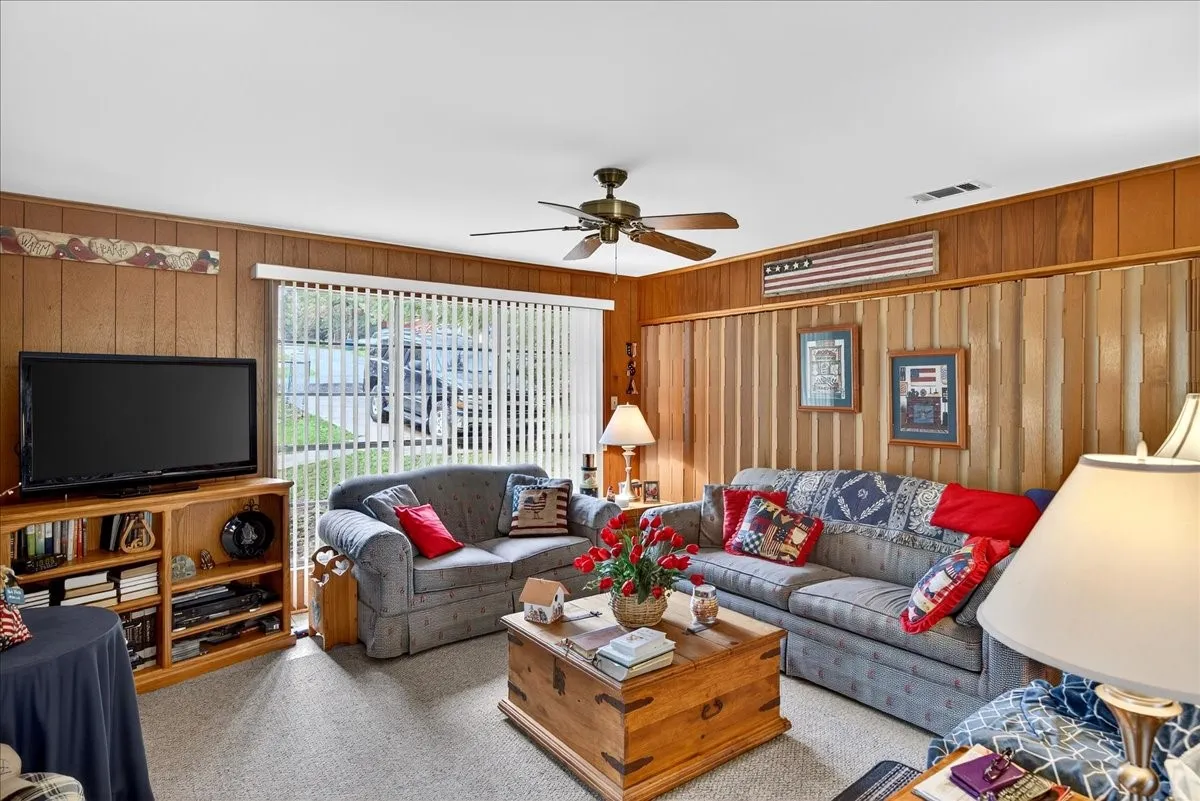 Living area with carpet, wood walls, and ceiling fan