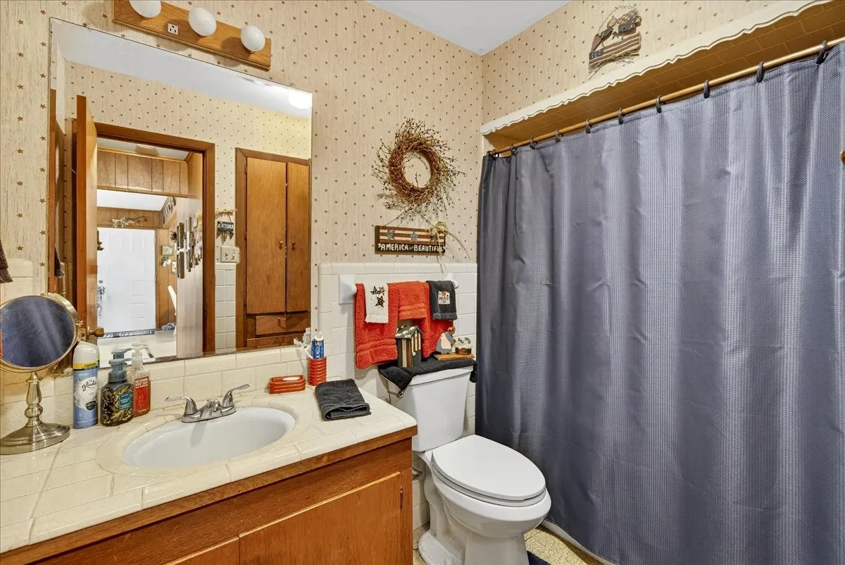 Bathroom with vanity, wallpapered walls, curtained shower, tile walls, and wainscoting