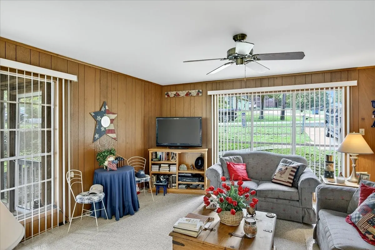 Carpeted living room with wood walls and ceiling fan
