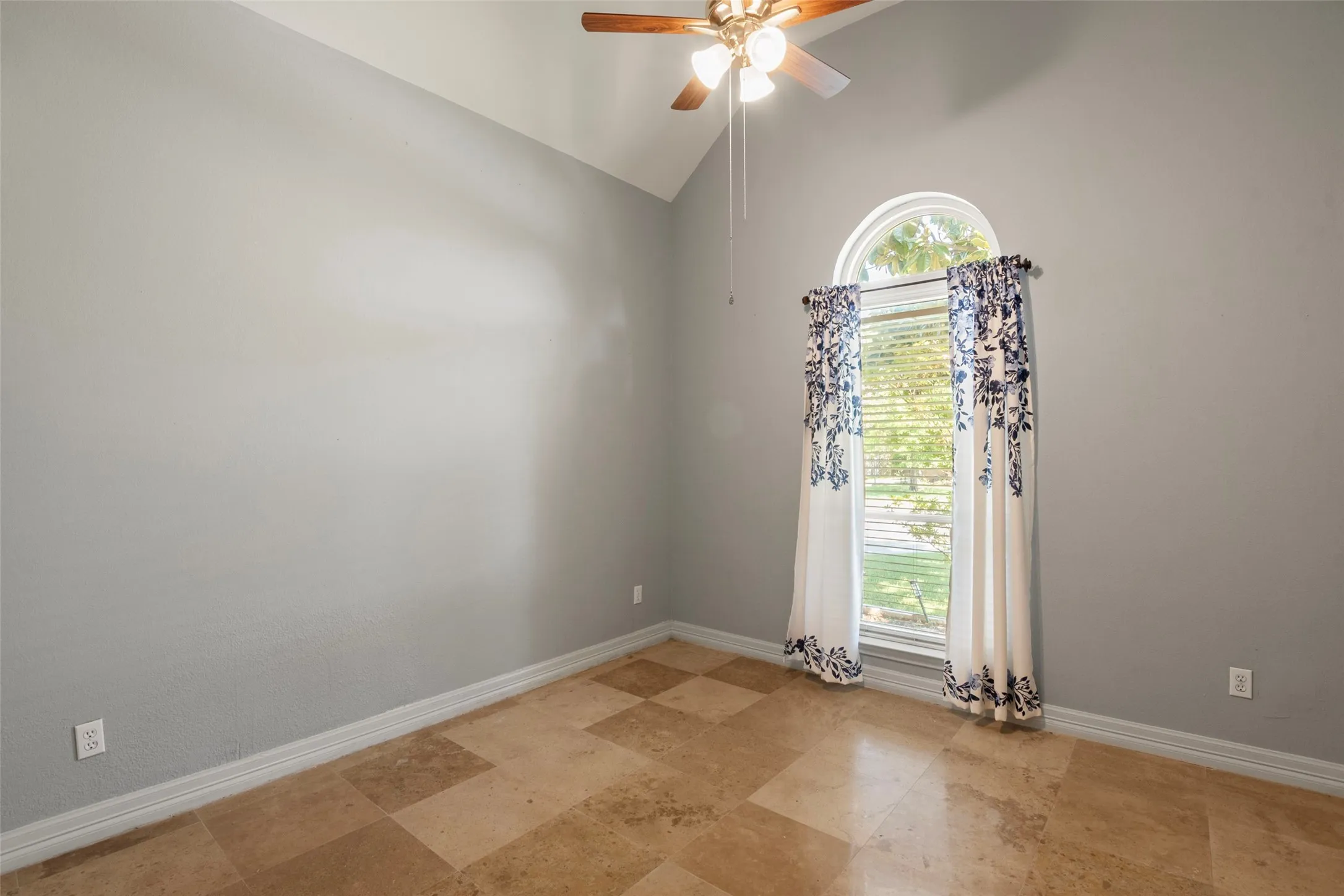 Vaulted ceiling with a ceiling fan, arched window, and checkerboard-patterned tile flooring