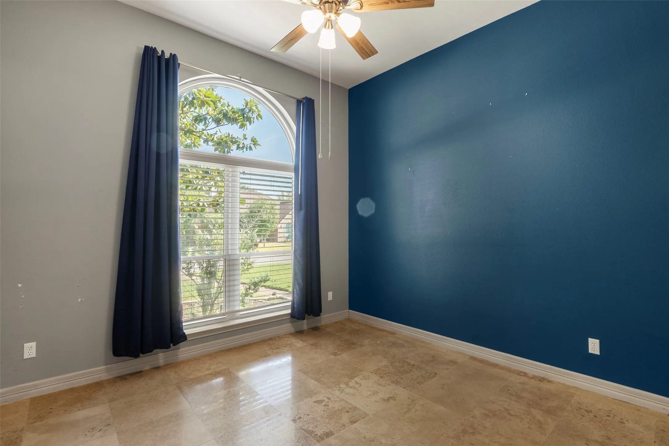 Arched window with blinds, tile flooring, ceiling fan, and accent wall