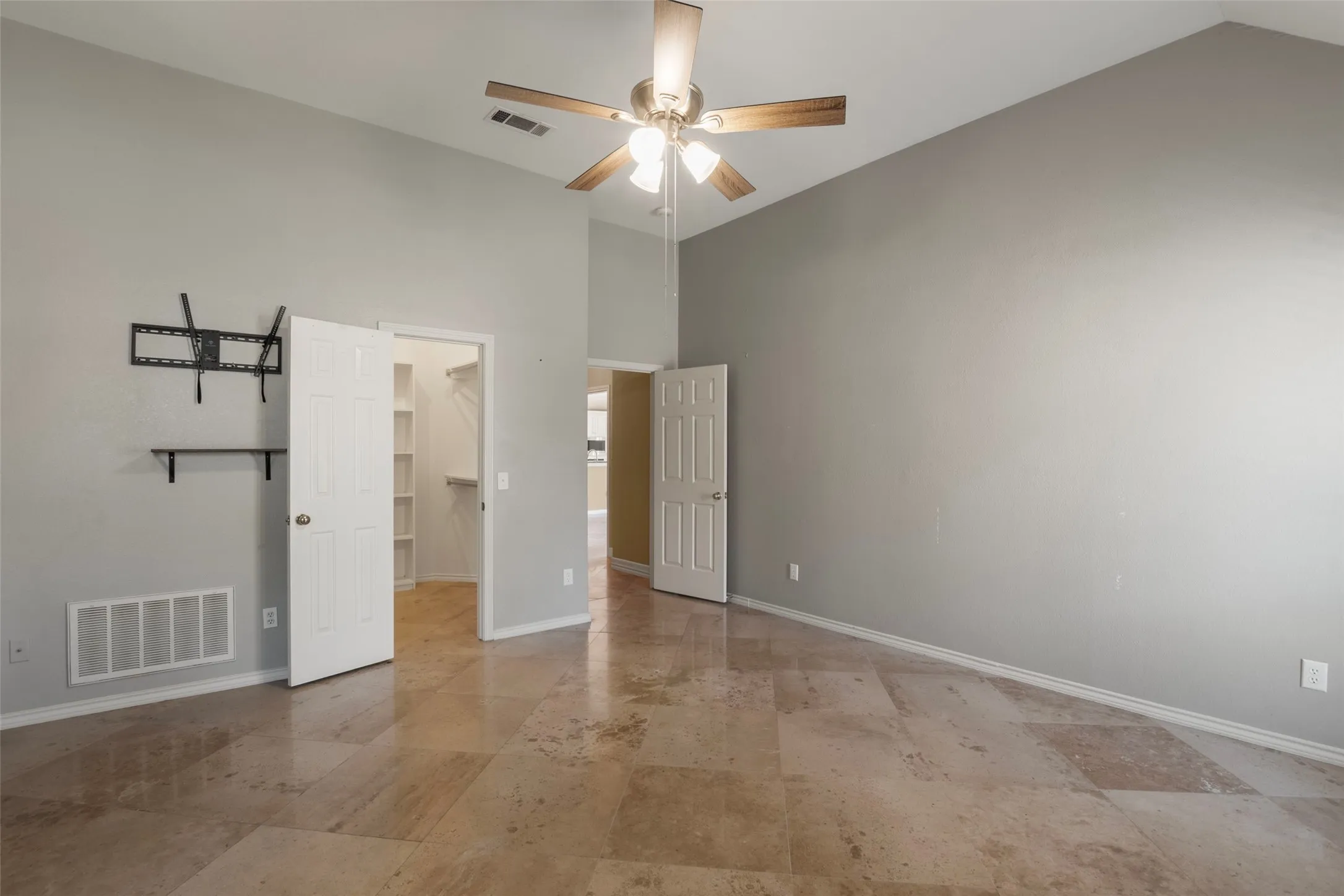 Vaulted ceiling with a ceiling fan, light-toned tiled flooring, and a walk-in closet with built-in shelving