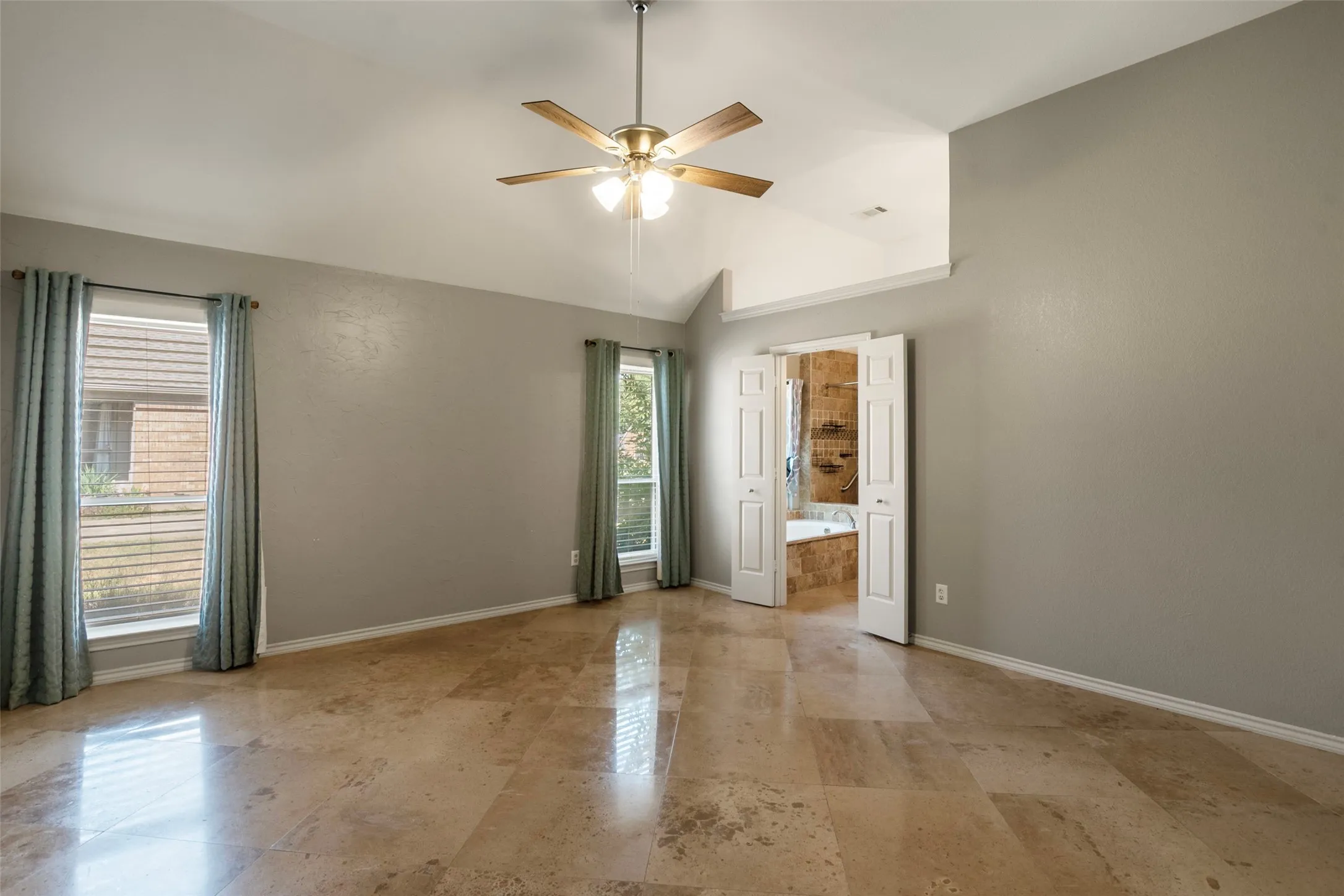 Vaulted ceilings, a ceiling fan with integrated lighting, two windows, and an en-suite bathroom with a built-in tub