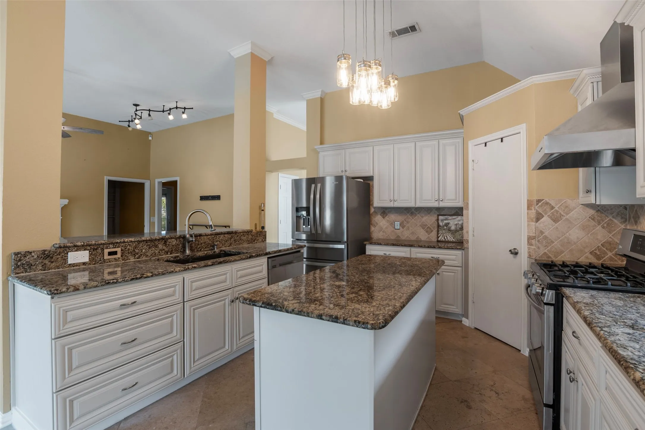 Kitchen featuring granite countertops, white cabinetry, stainless steel appliances, a center island, and vaulted ceilings