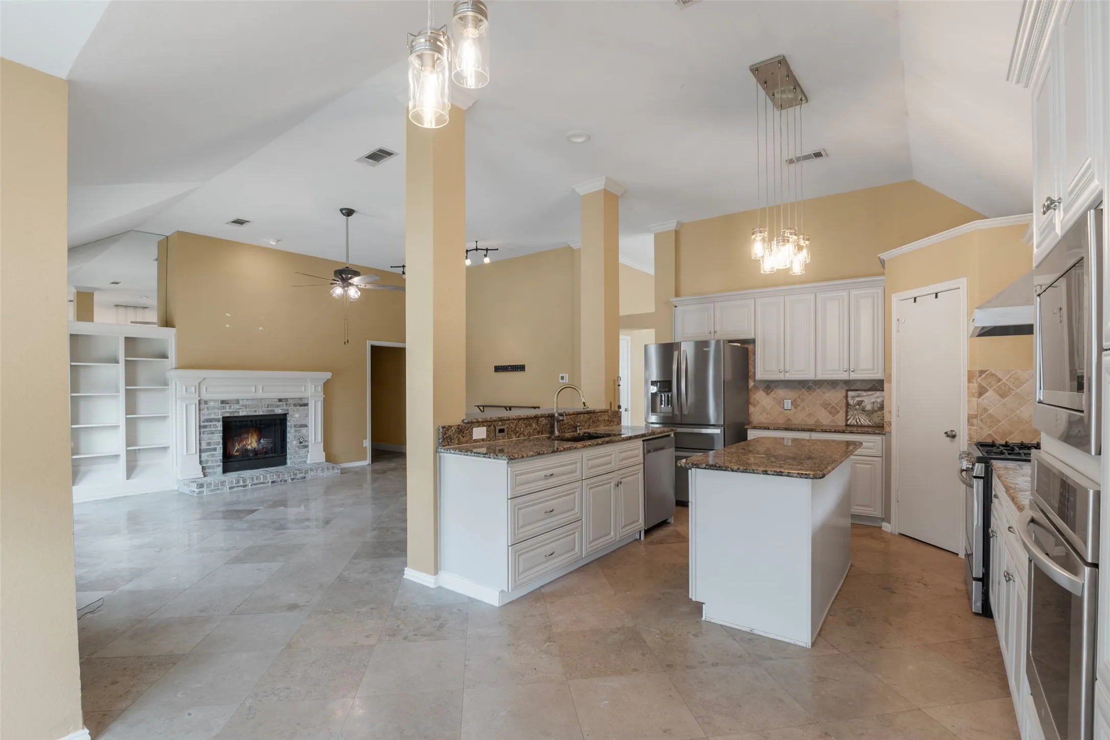 Vaulted ceiling, built-in shelving, stone fireplace, kitchen island, and stainless steel appliances