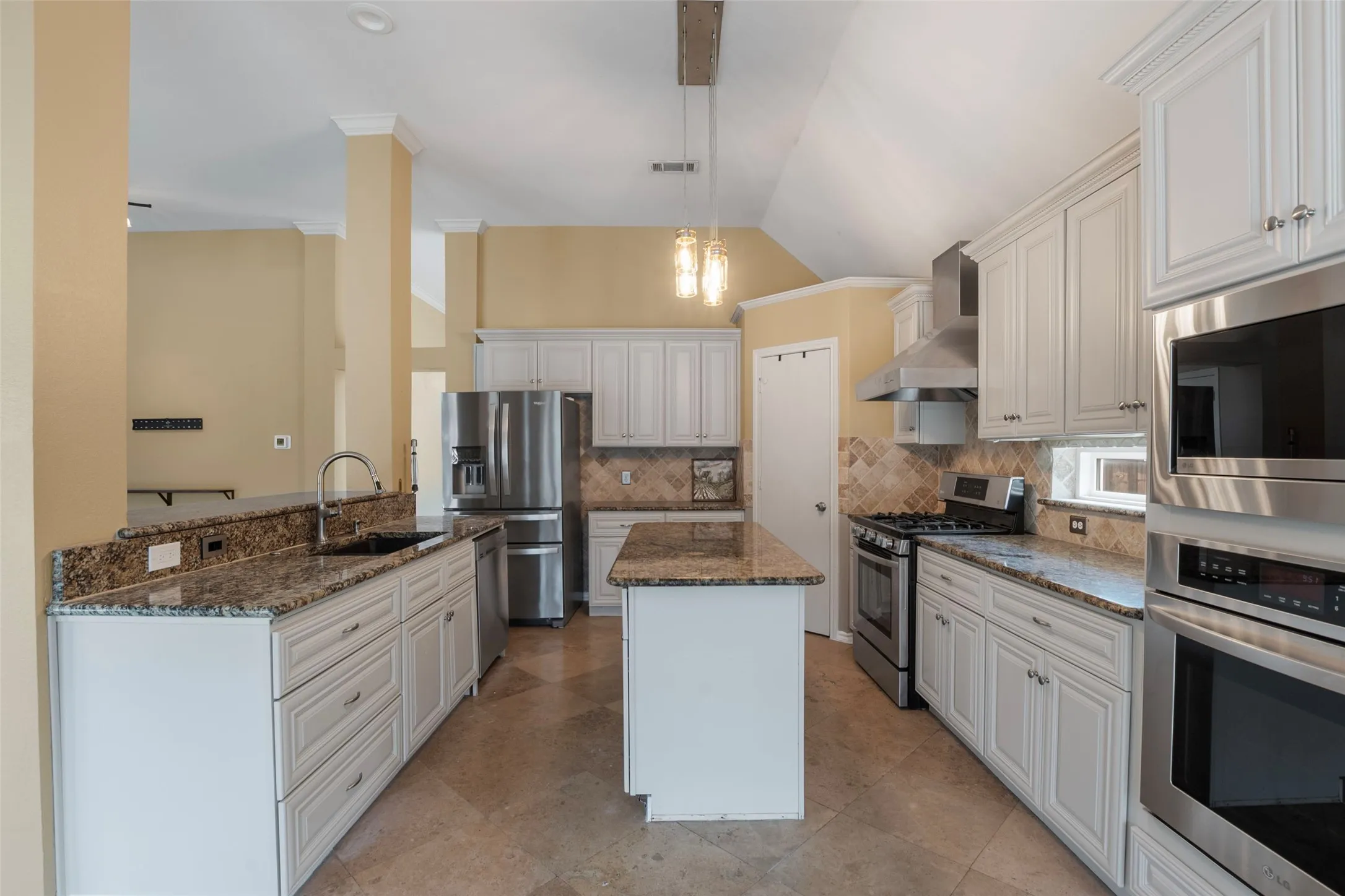 Kitchen featuring an island, white cabinetry, integrated stainless steel appliances, granite countertops, and tile flooring