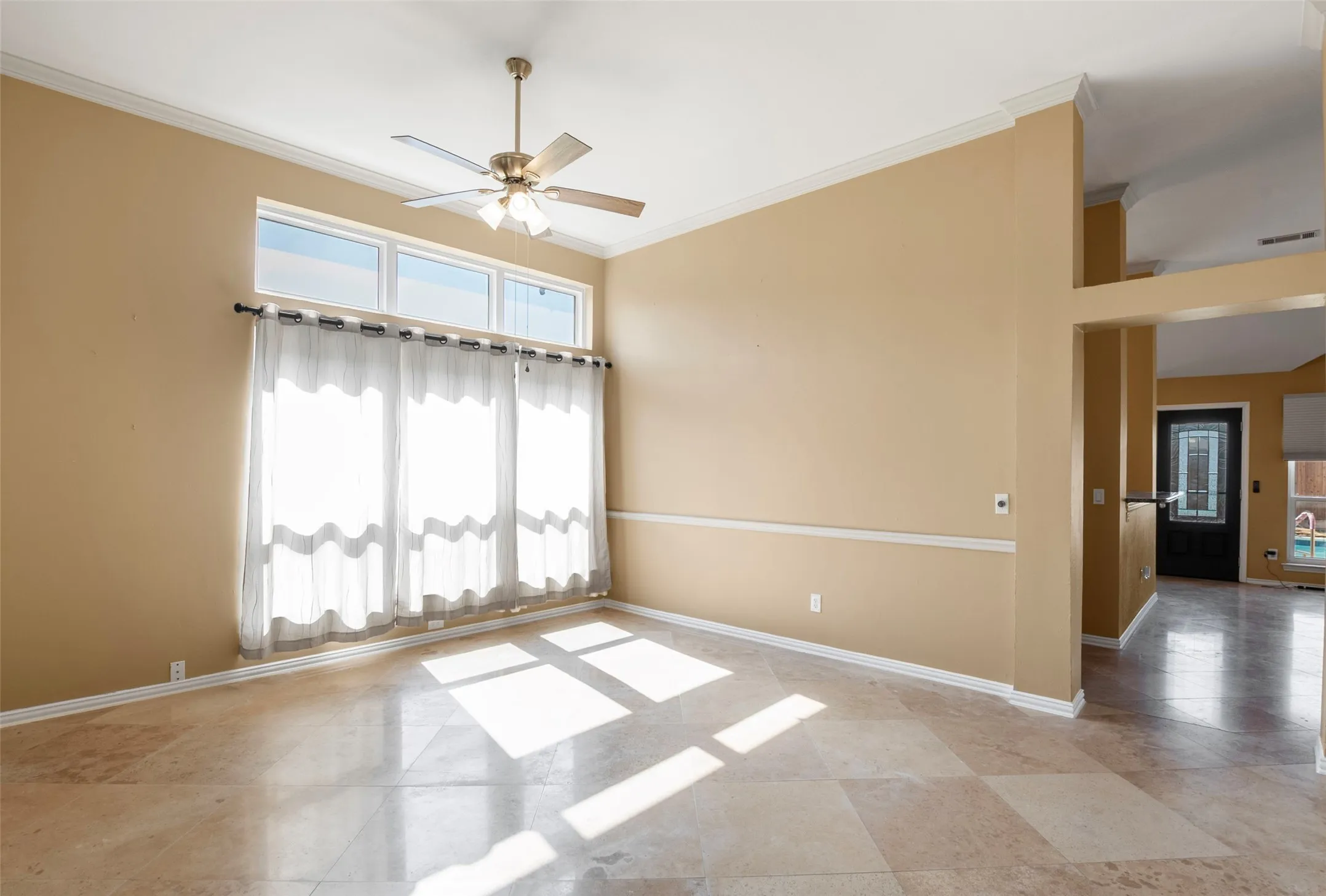 Vaulted ceiling with crown molding, ceiling fan, transom windows, ceramic tile flooring, and decorative chair rail