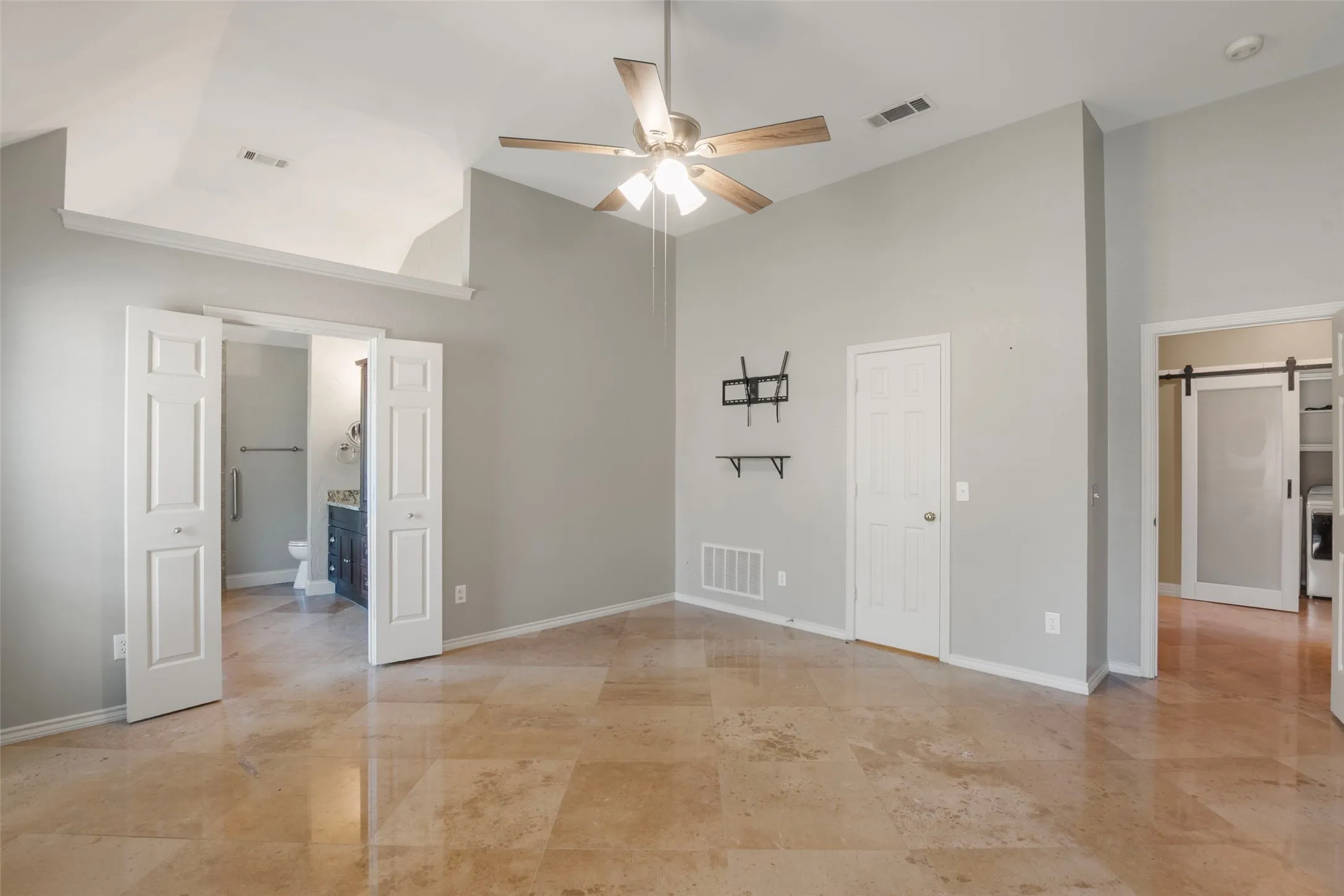 Vaulted ceiling with a ceiling fan, stone tile flooring, and a sliding barn door