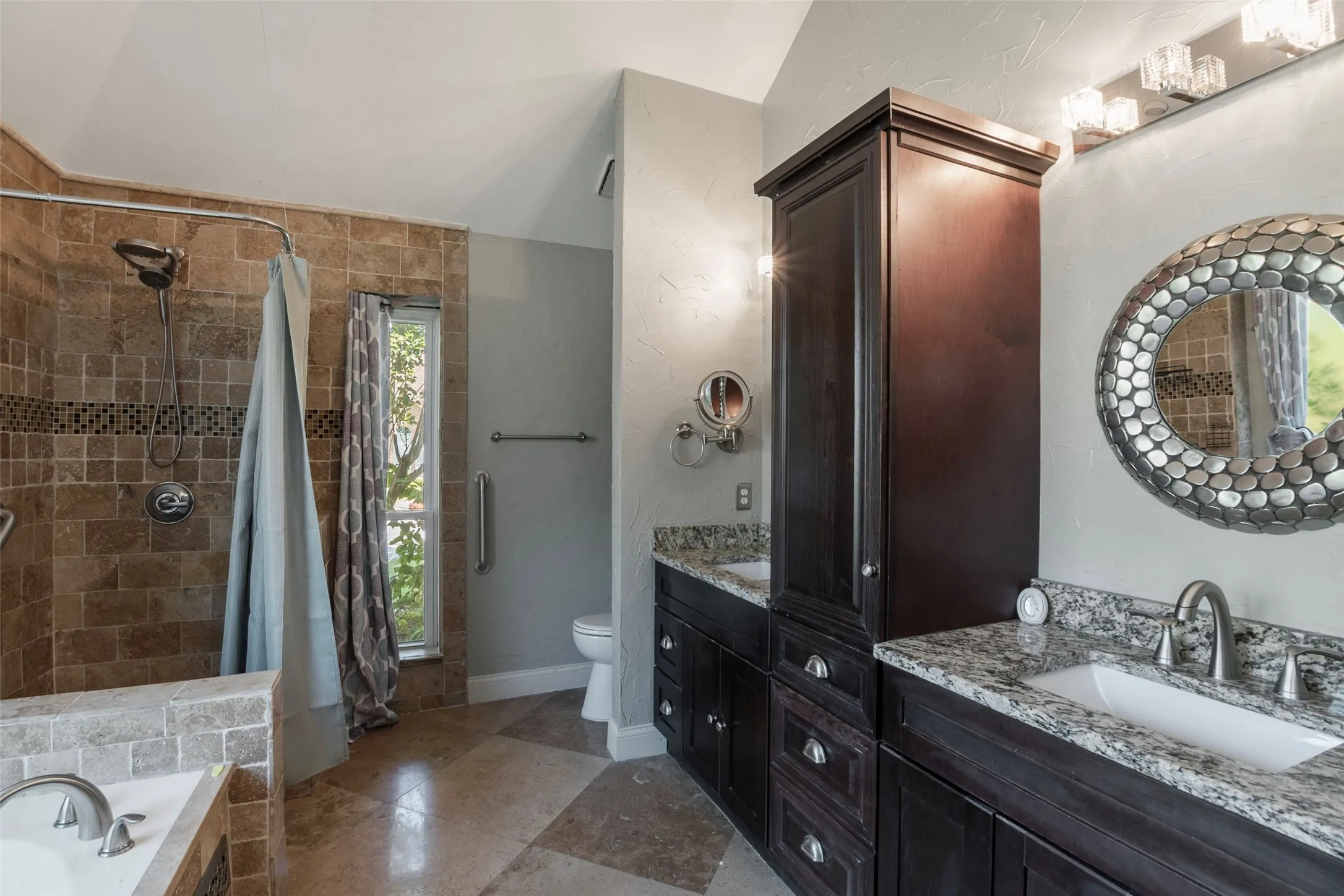 Dual vanity with granite countertops, tile flooring, built-in storage cabinet, tiled shower, and a separate toilet area