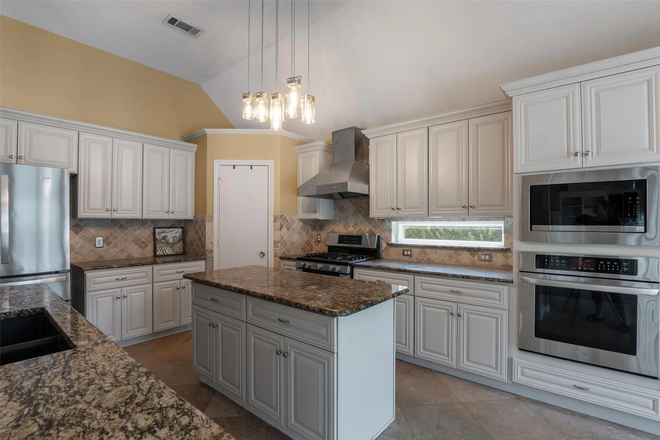 White cabinetry, stone countertops, stainless steel appliances, central island, and vaulted ceiling