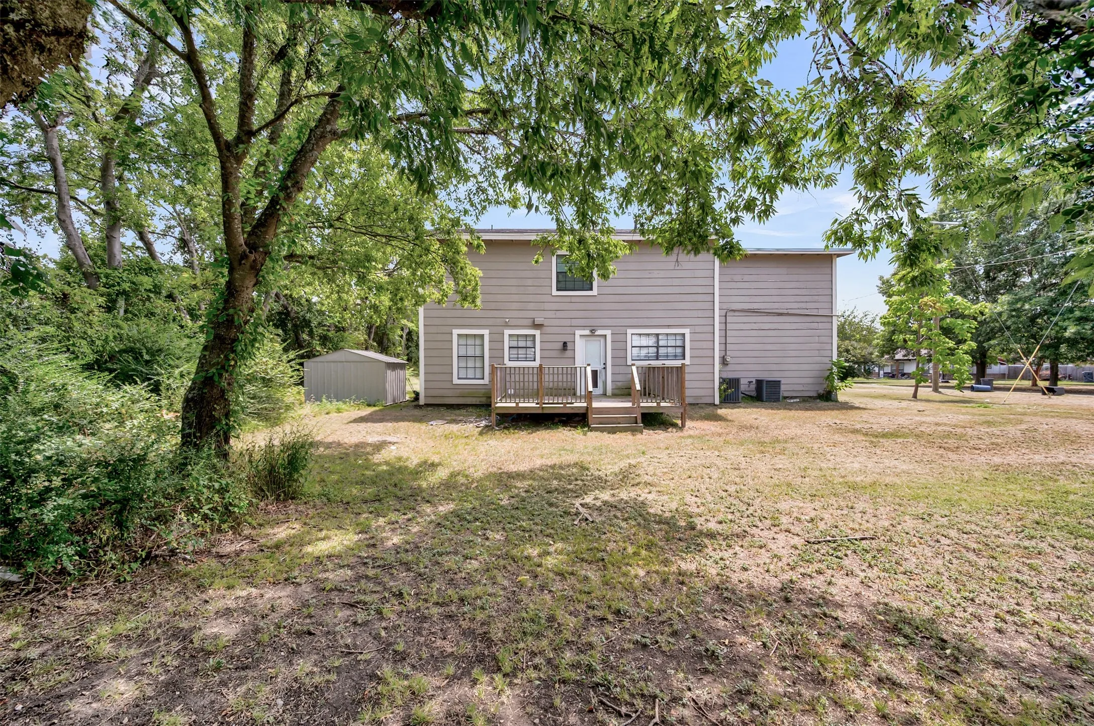 Back of house with a wooden deck, a storage unit, and a yard