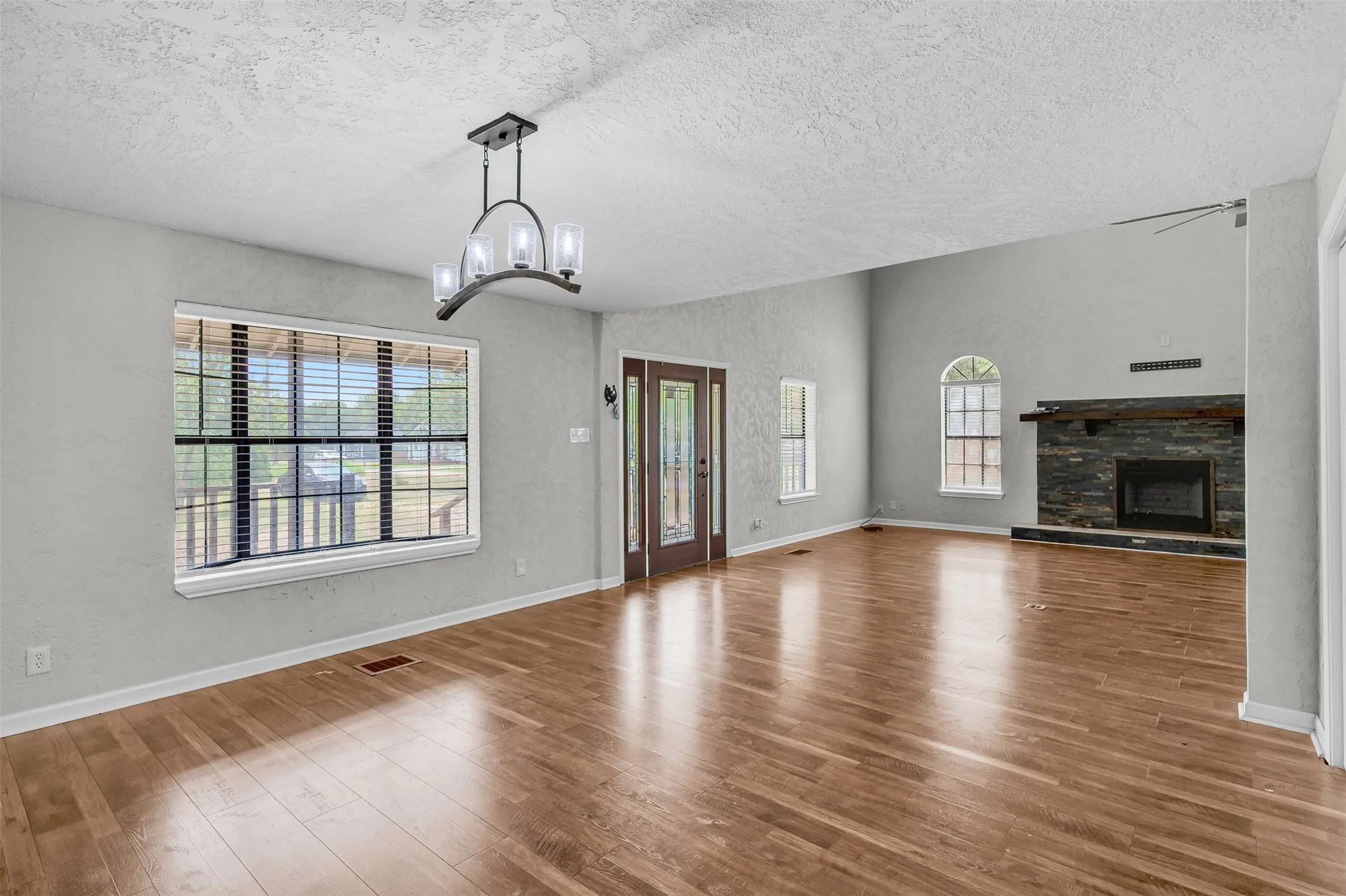 Unfurnished living room featuring wood finished floors, a textured ceiling, a stone fireplace, a textured wall, and a chandelier